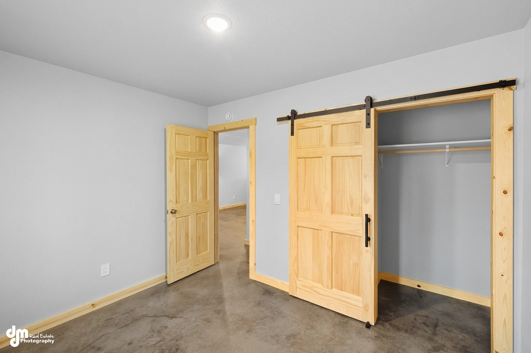 Empty bedroom with light wooden doors, including a sliding barn door that leads to a closet, with a gray wall and carpeted floor.