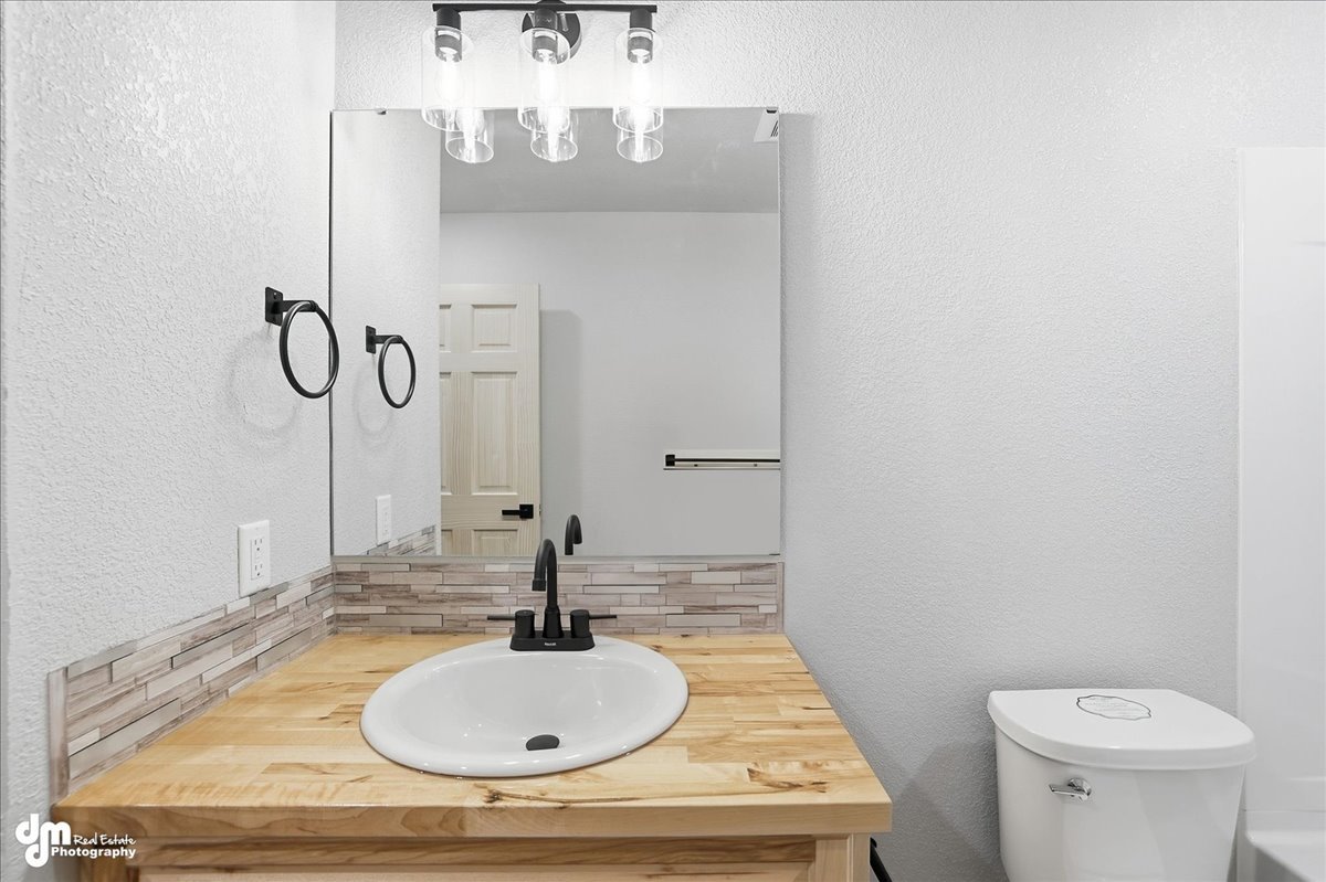 Bathroom with a wooden vanity, white sink, black faucet, mirror, two black ring towel holders, and a white toilet.