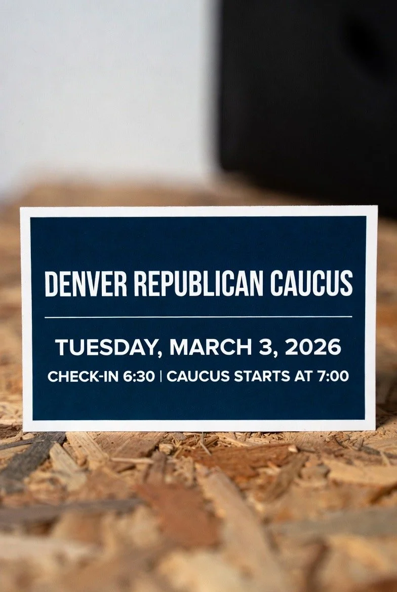 A sign for the Denver Republican Caucus with the date Tuesday, March 3, 2026, and check-in times at 6:30 and caucus start at 7:00, placed on a wooden surface.