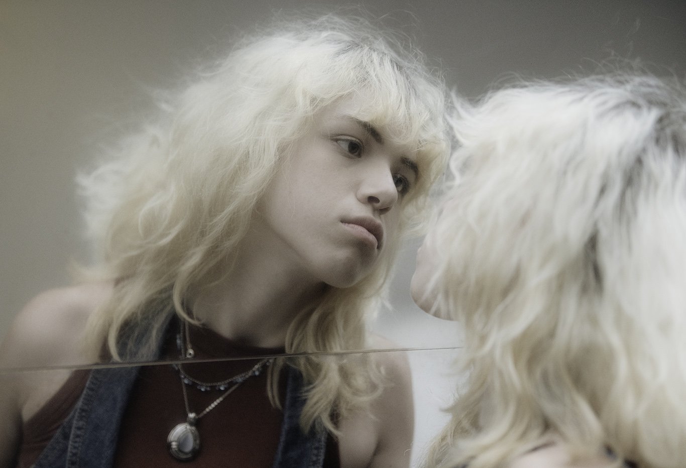 Young woman with platinum blonde hair looking at her reflection in a mirror.