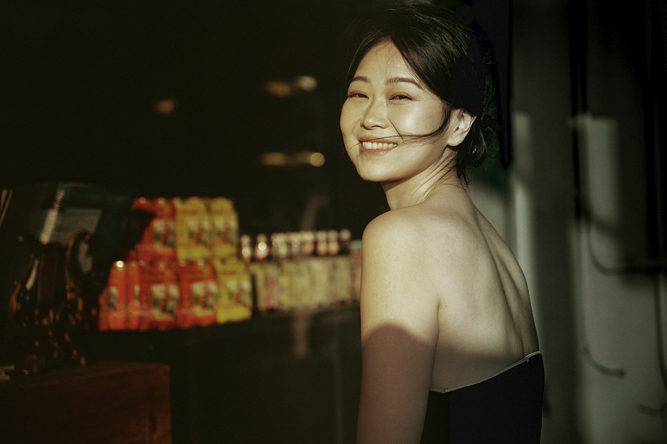 Woman smiling and winking with short black hair wearing a black strapless top in a dimly lit environment with snacks.