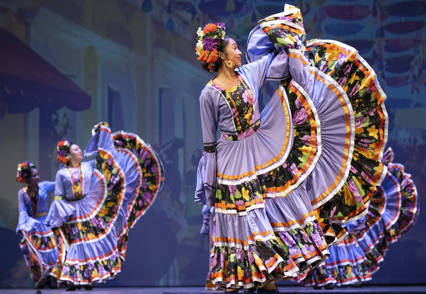 Group of women performing Mexican folkloric dance in colorful embroidered dresses with flower crowns.