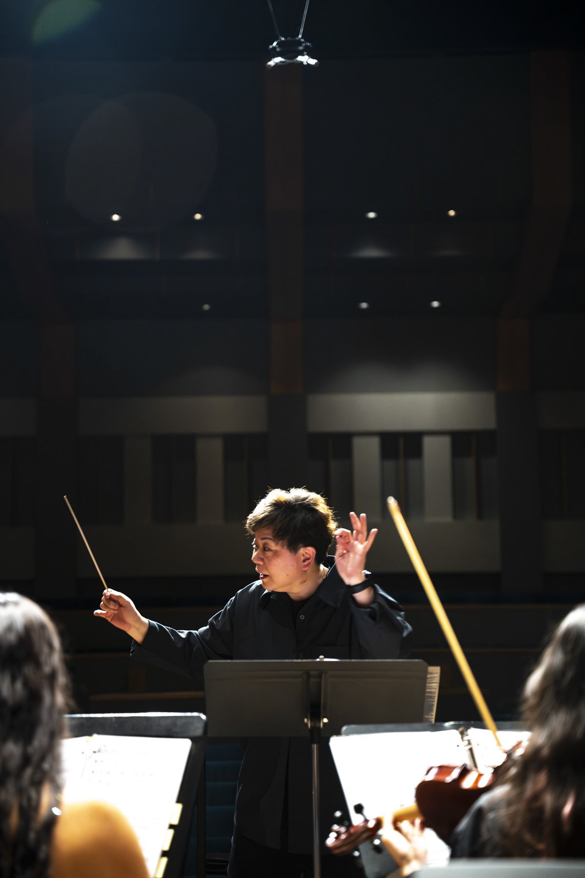Orchestra conductor leading musicians during rehearsal or performance in dark concert hall.