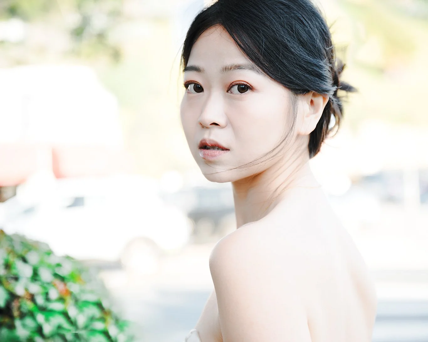Portrait of young Asian woman with short black hair and natural makeup looking over her shoulder outdoors.