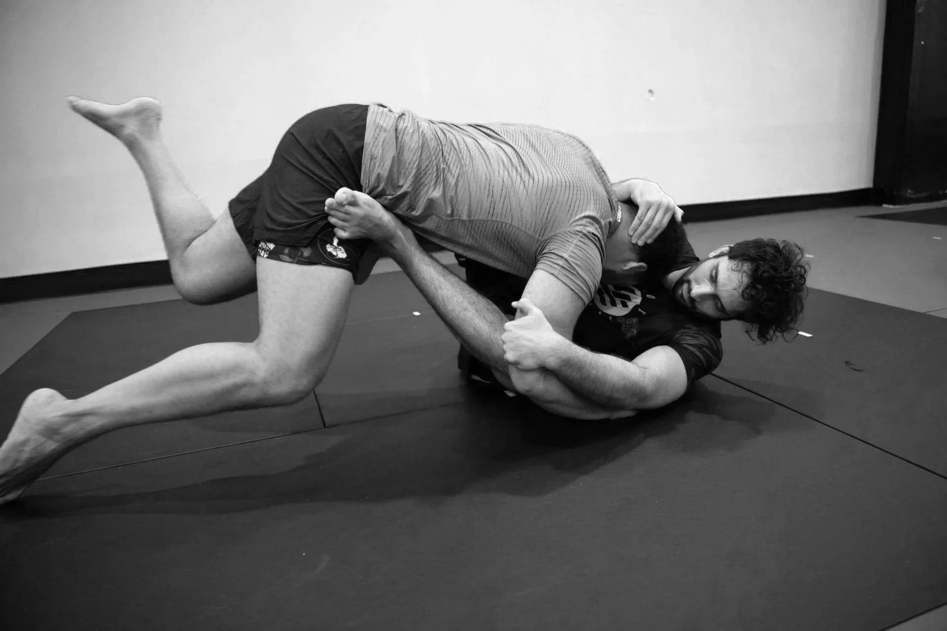 Two adults practicing Brazilian Jiu Jitsu on mats in a jiu jitsu gym located in Brooklyn Heights