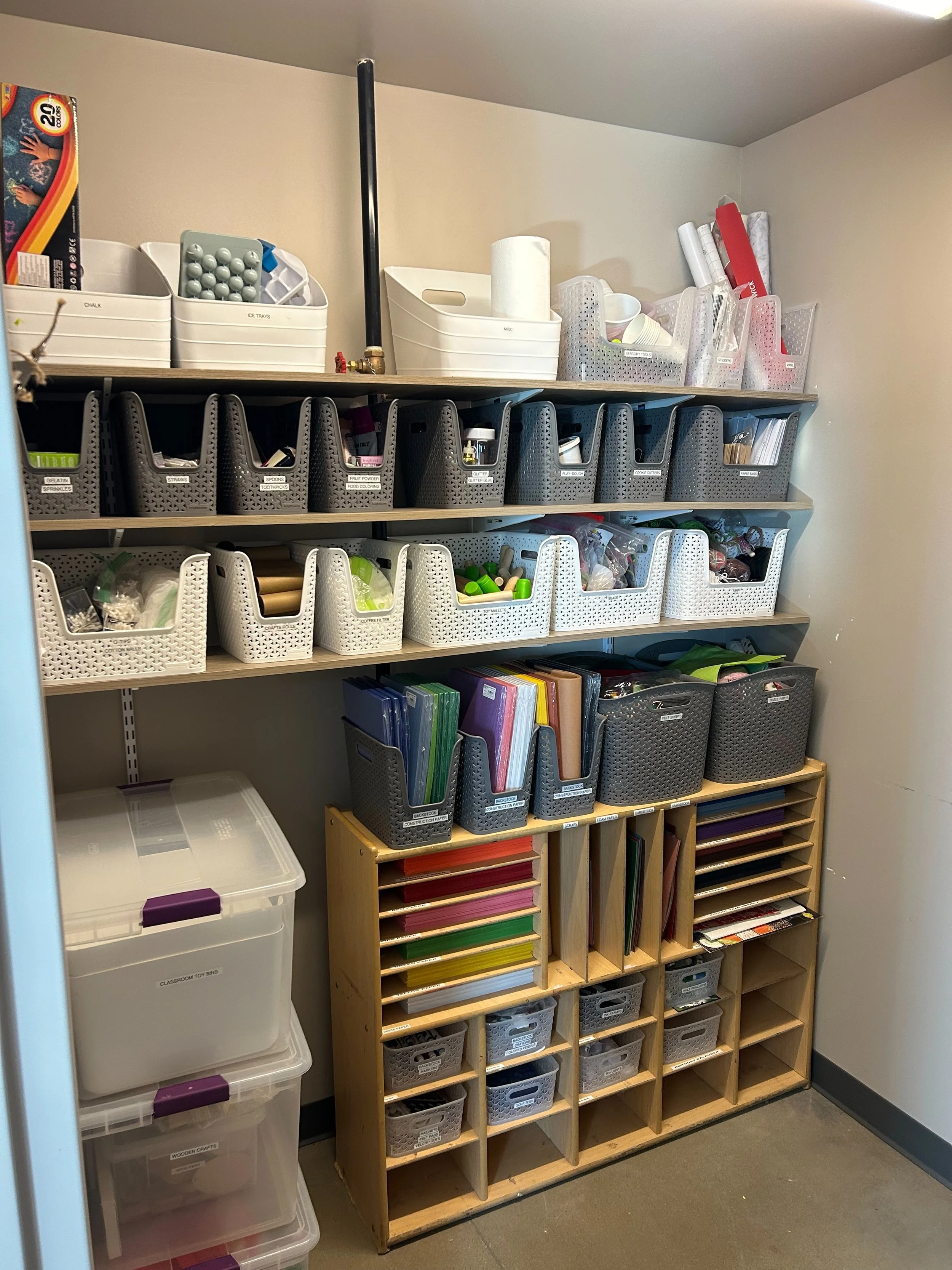 Storage room with shelves containing various labeled boxes and containers holding office supplies, craft materials, and organizational items.