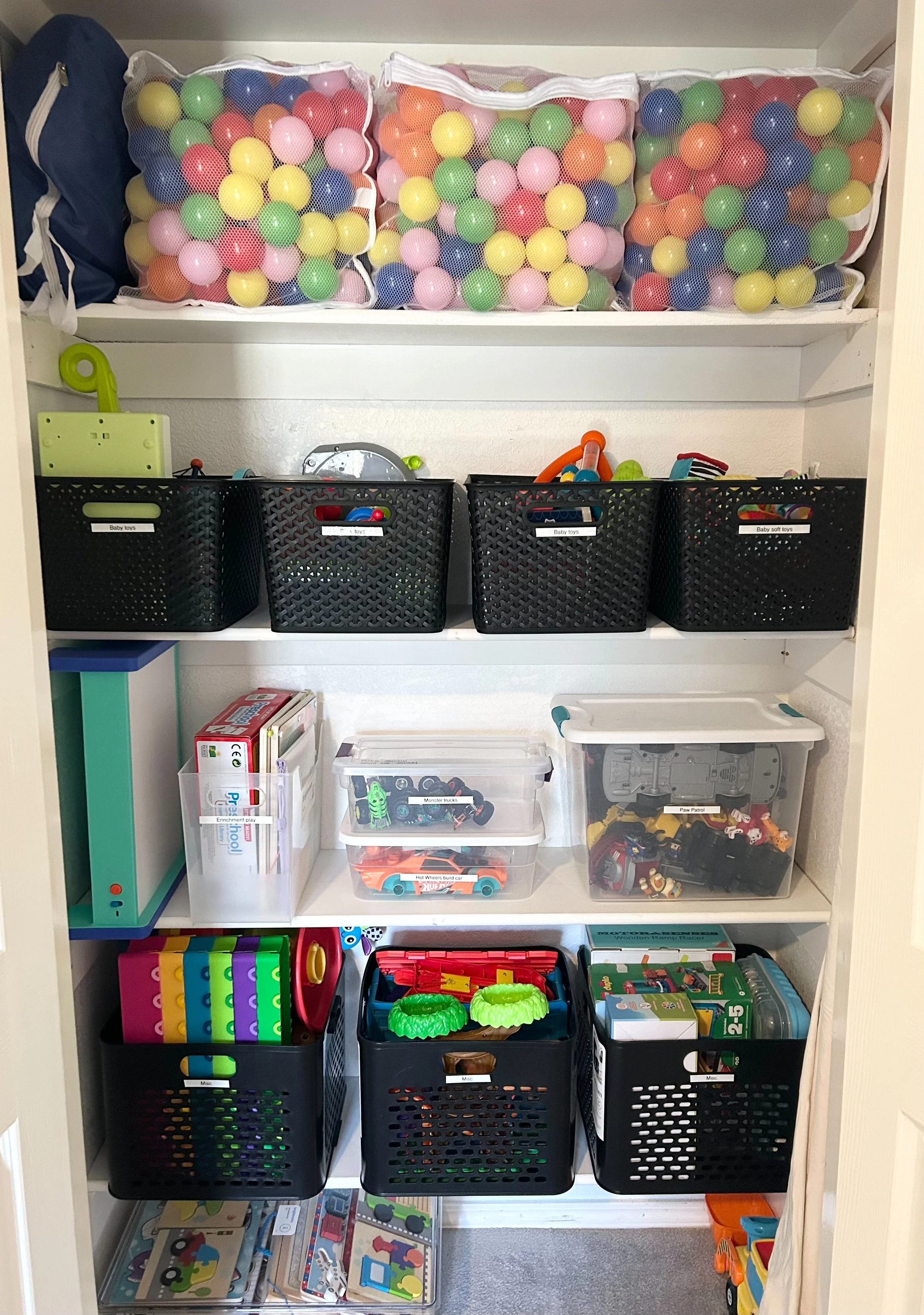 A children's toy storage closet filled with assorted toys in baskets and containers, including colorful balls, toy cars, games, and plush figures.