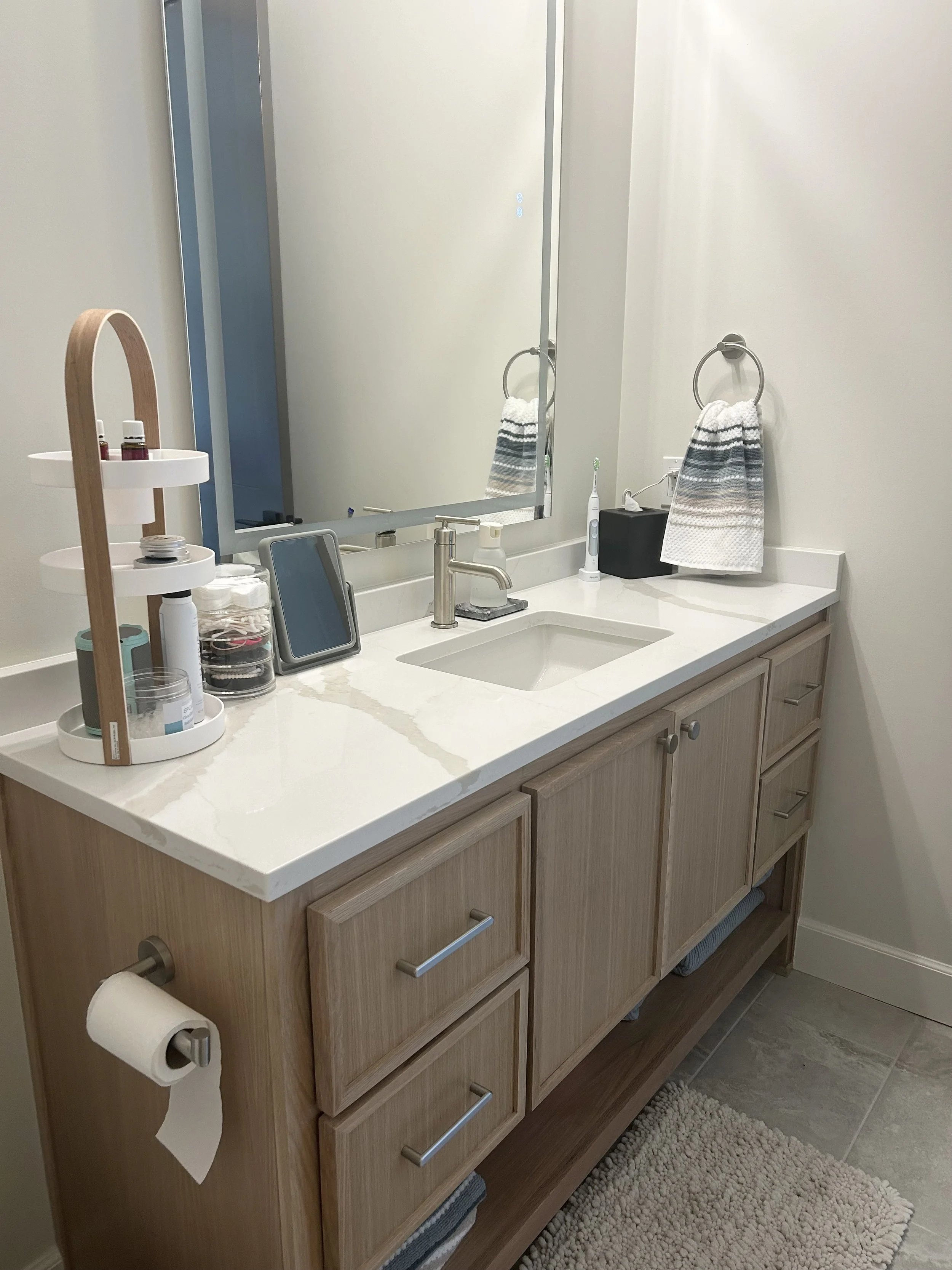 Bathroom vanity with a marble countertop, mirror, and various toiletries, including a toothbrush, hand soap, towel, and storage containers.