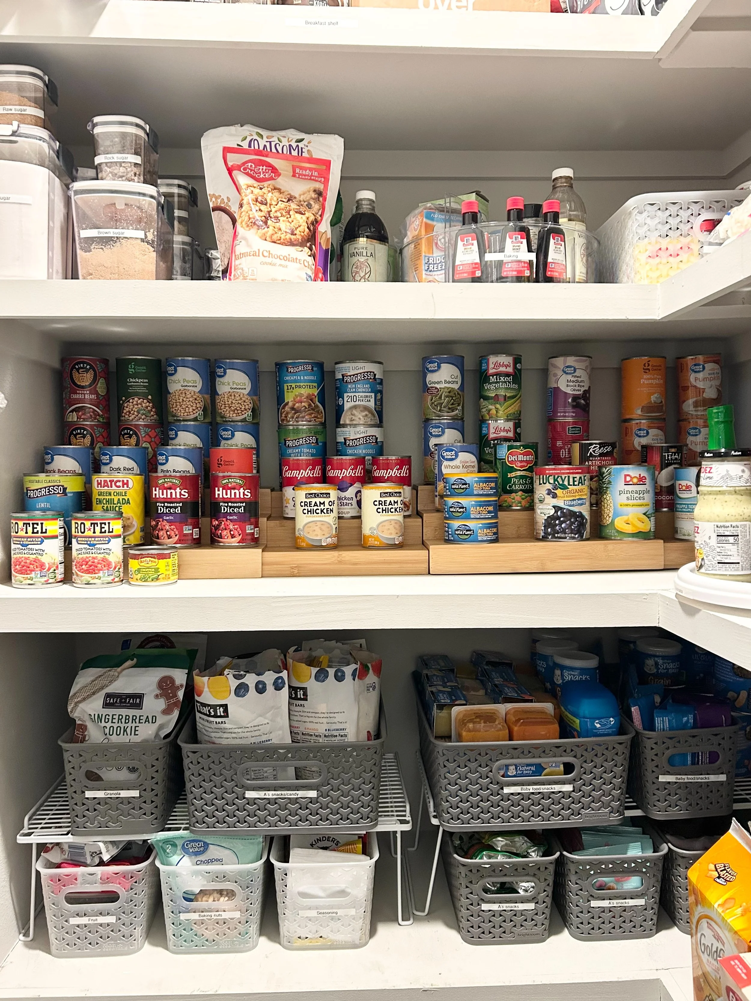 Organized pantry with canned goods on the middle shelf, snack baskets on the bottom, and baking supplies at the top.