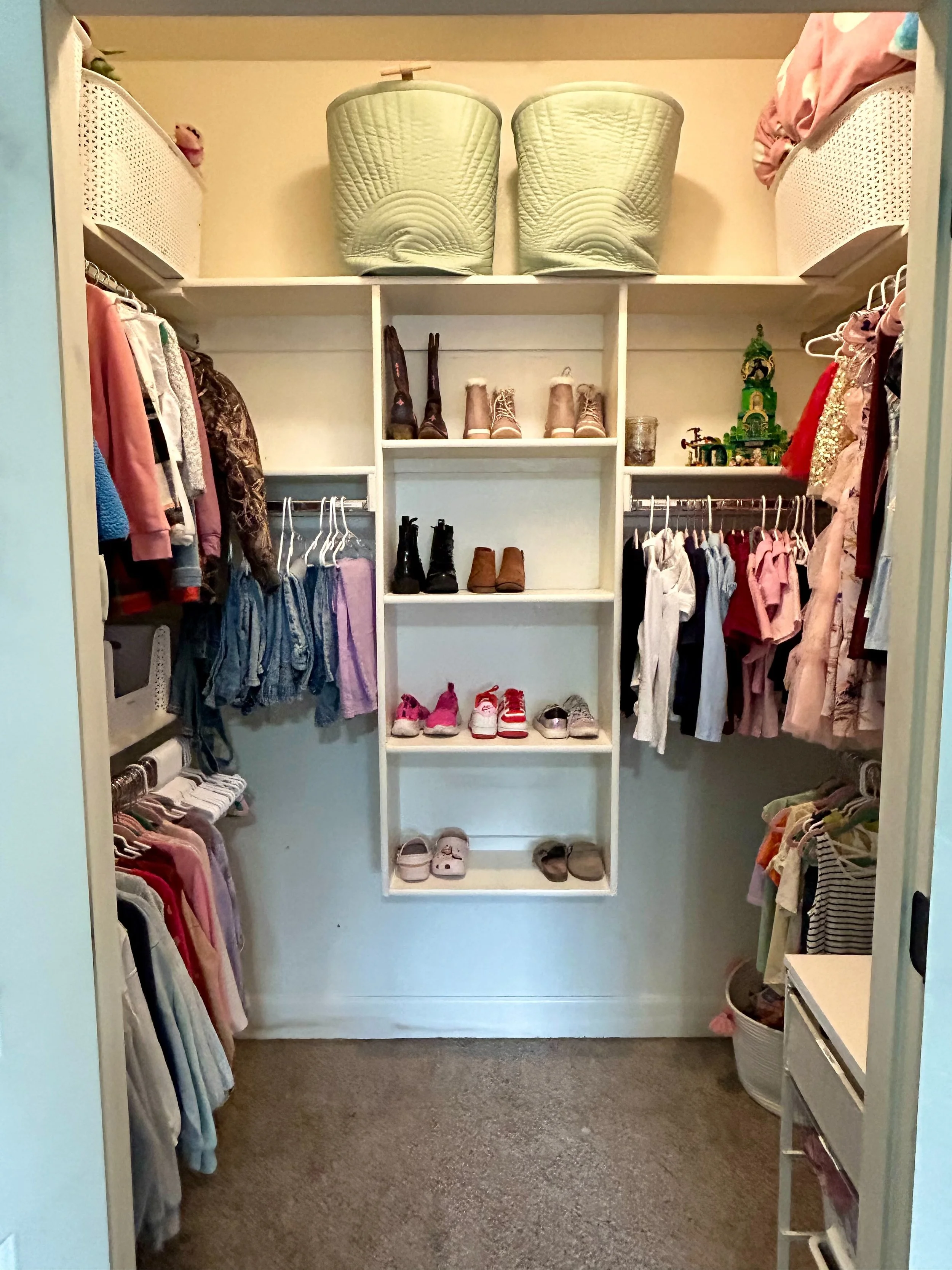 A walk-in closet with clothes on hangers and shelves, organized with shoes, boots, toys, and storage baskets.