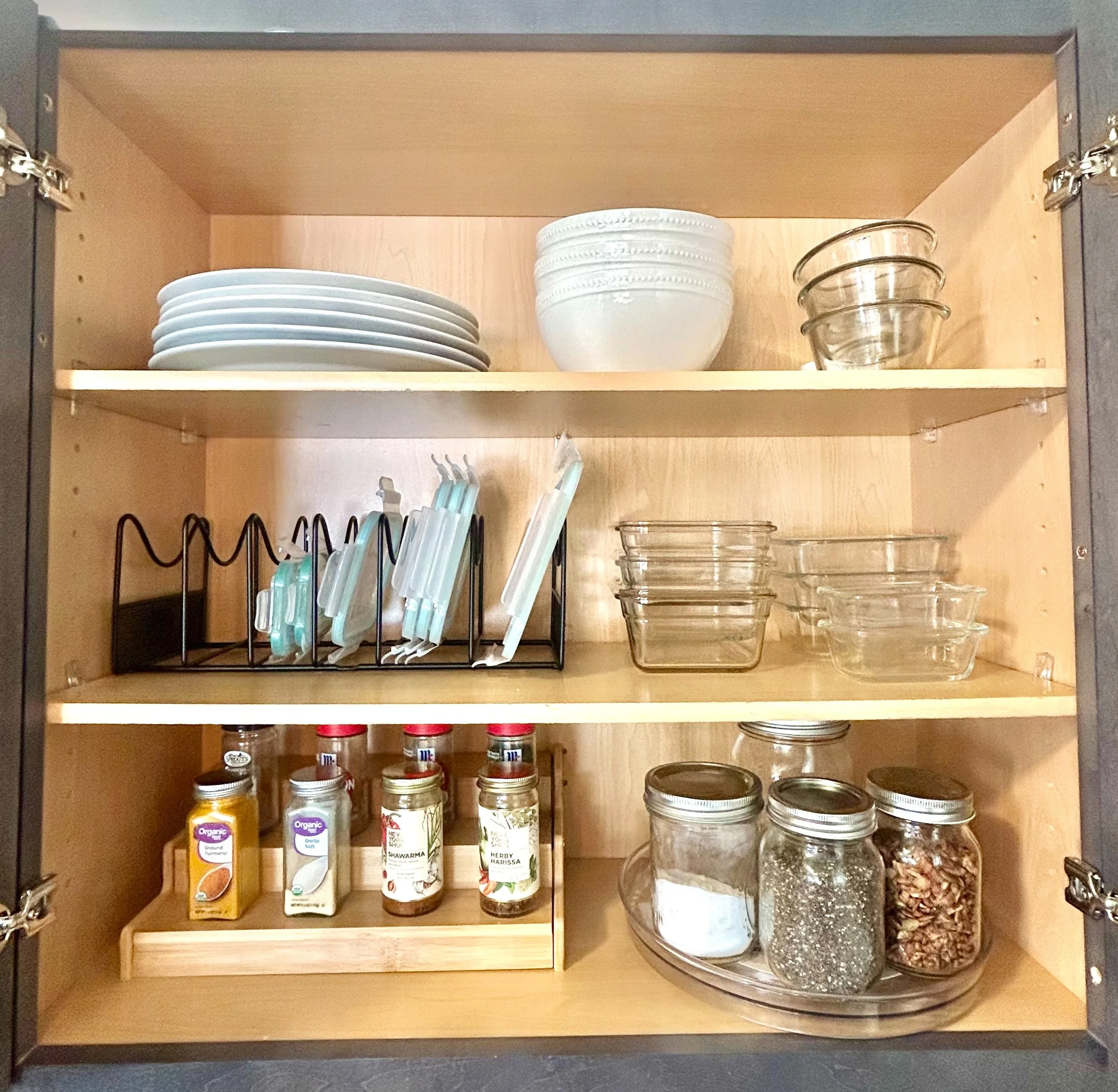 View of a kitchen cabinet with dishes, glassware, spices, and baking ingredients organized on shelves.