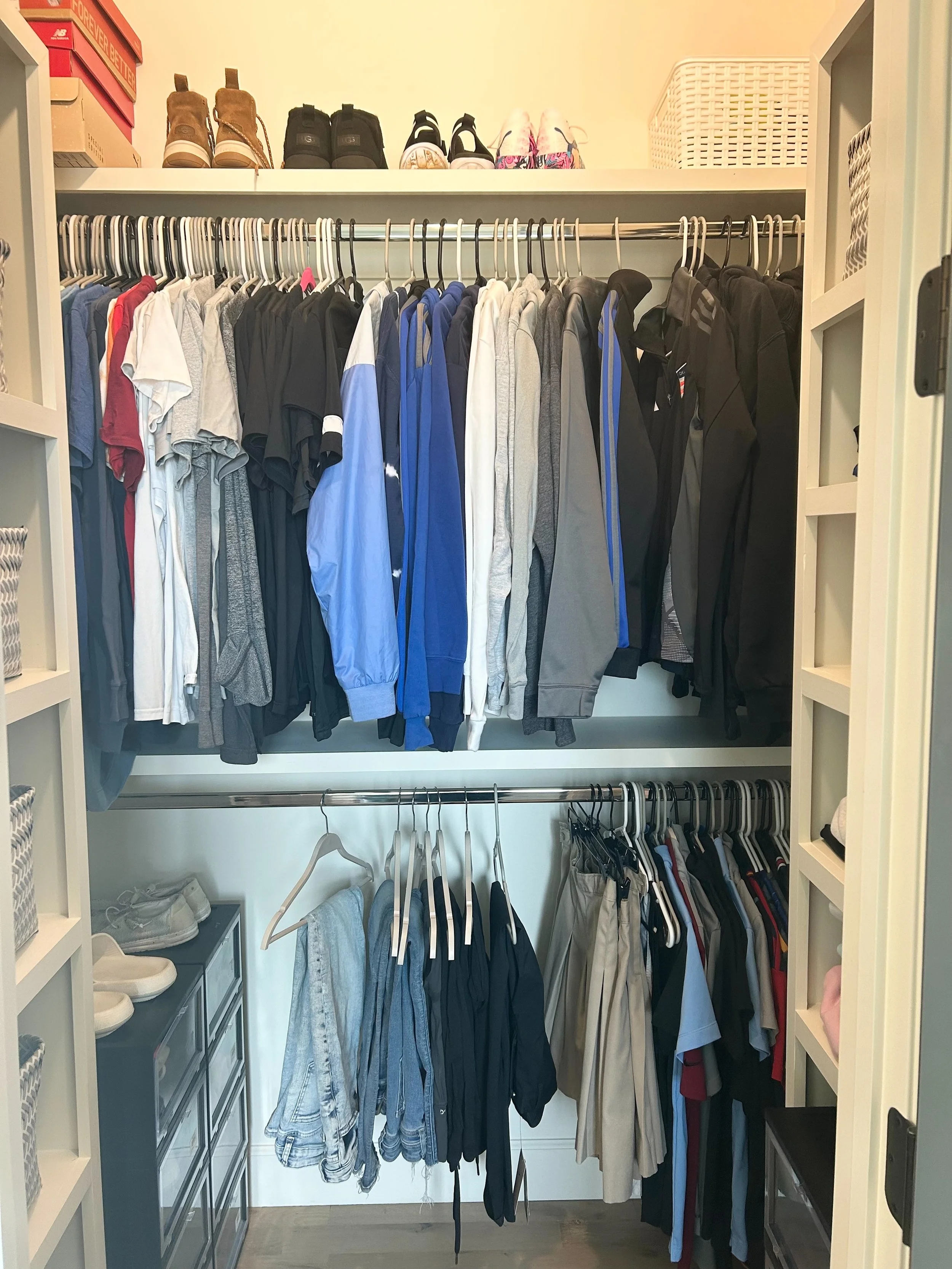 A closet with organized clothes on two hanging rods, shoes and boxes on a top shelf, and storage drawers on the side.