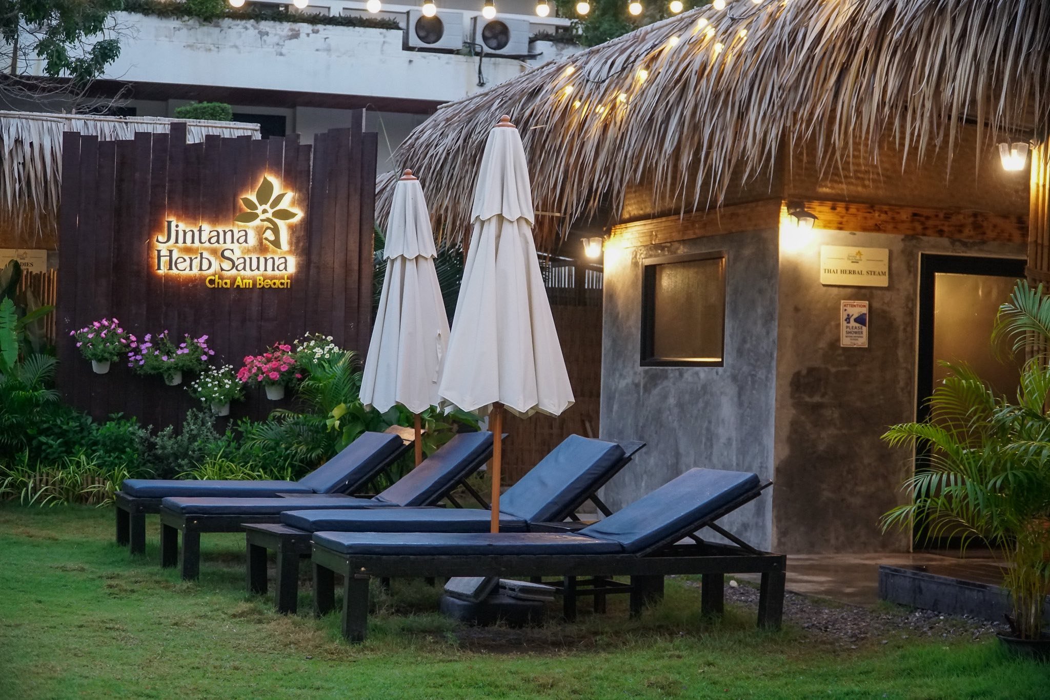 Tropical outdoor bar with thatched roof at beach, surrounded by trees and colorful sunrise sky with blue, yellow, and orange hues.
