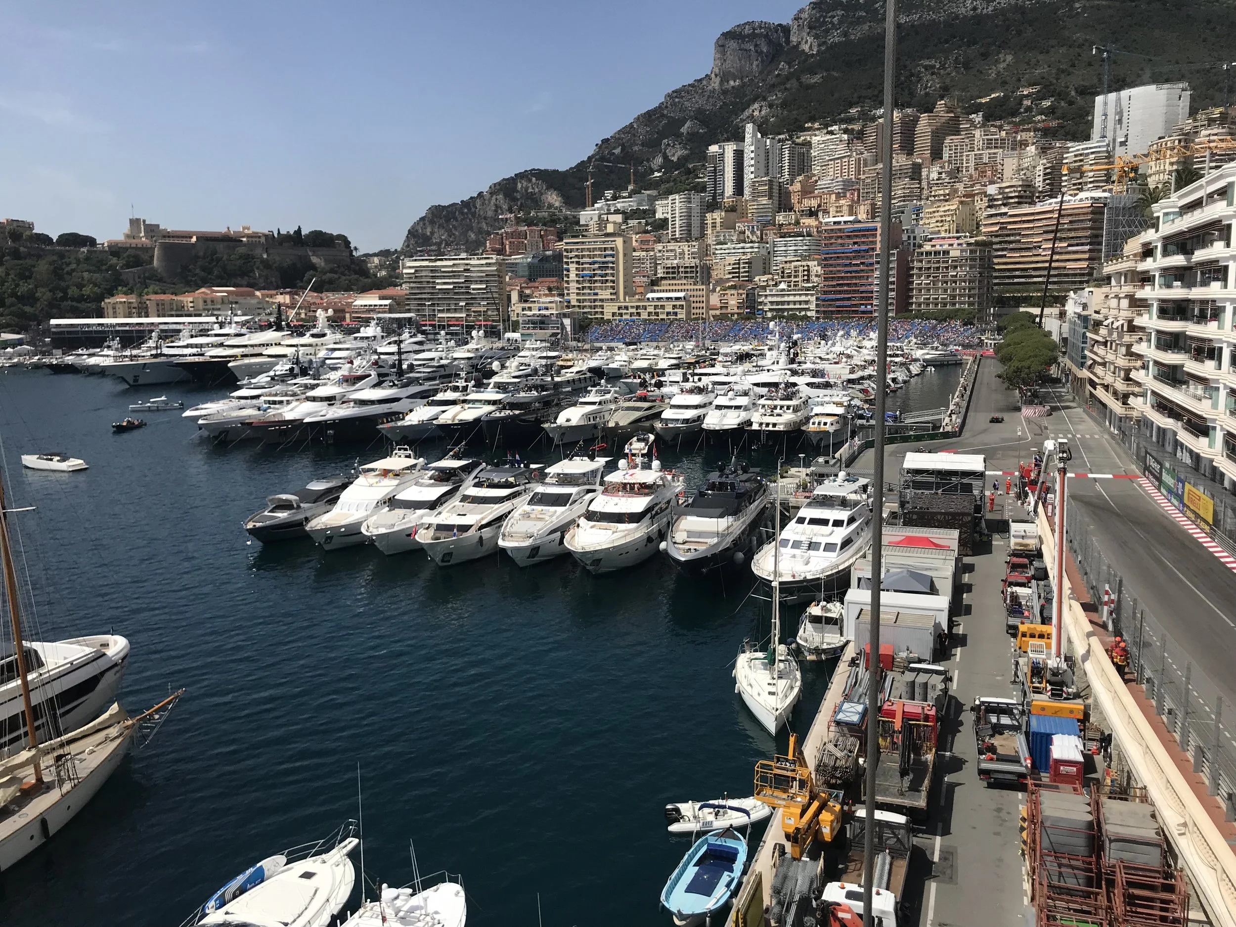 A marina filled with numerous yachts and boats docked, with a cityscape and hillside in the background.