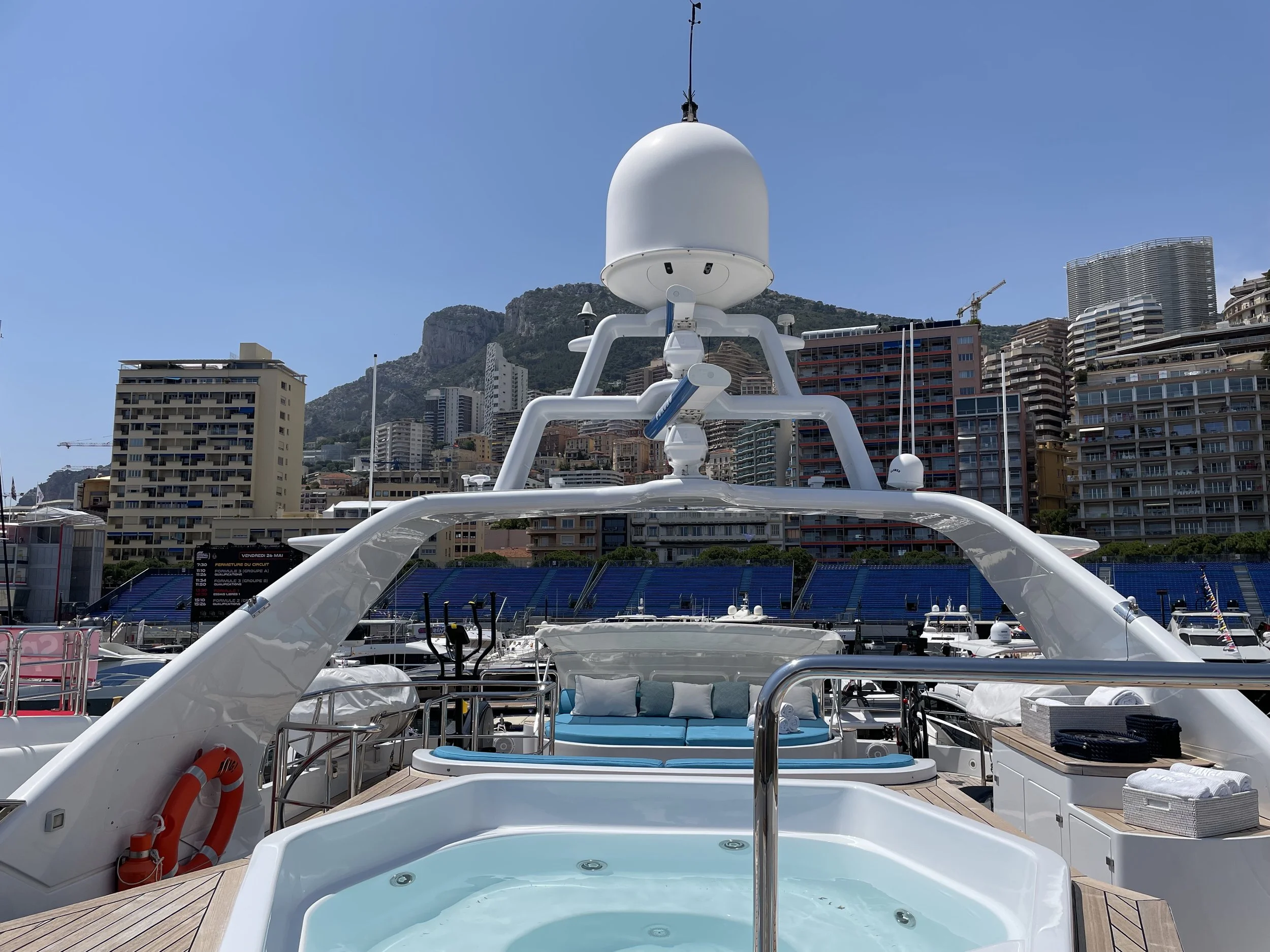 Luxury yacht docked at a marina with a city skyline and mountains in the background.