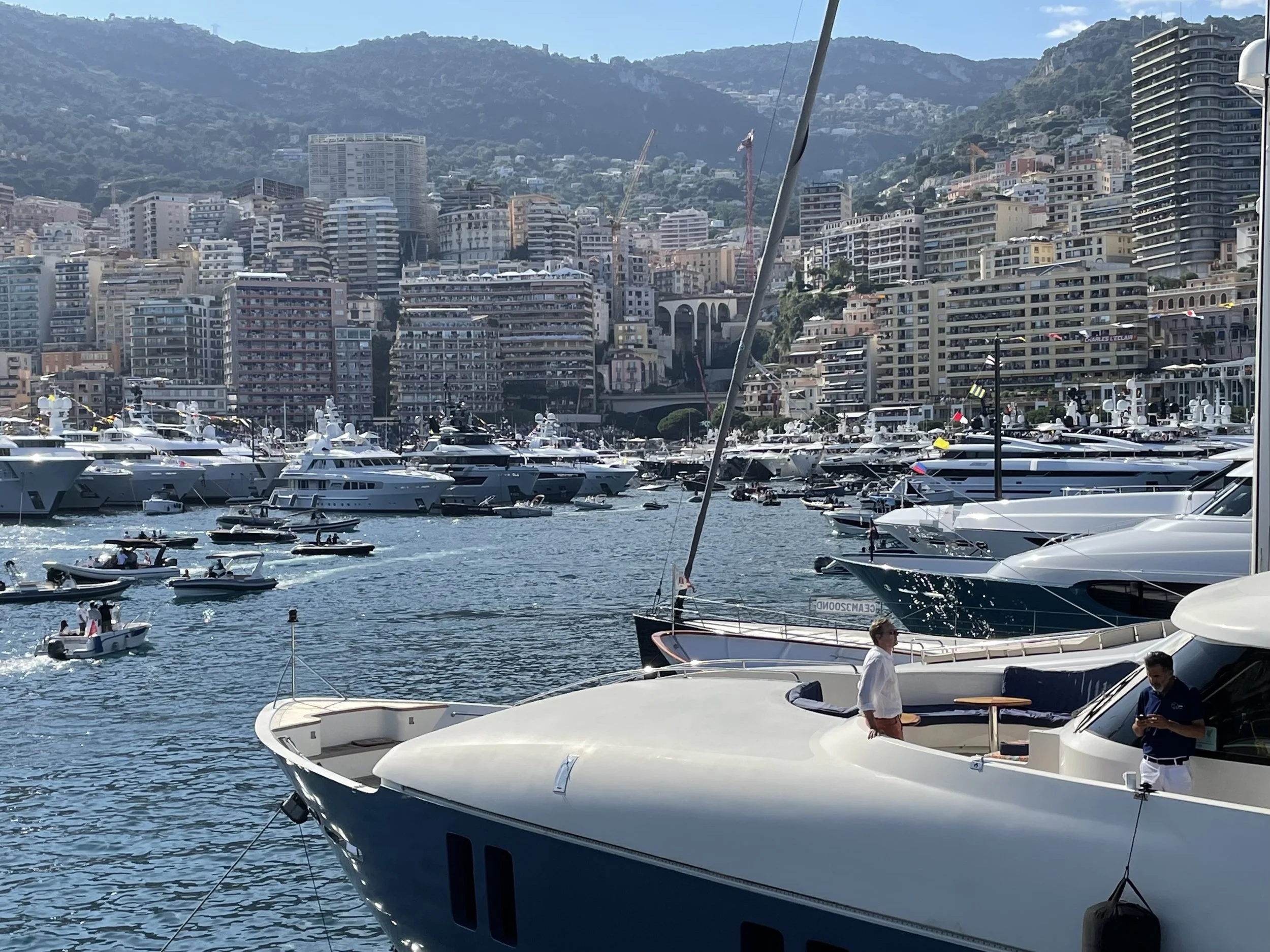 Marina filled with luxury yachts and boats, with a cityscape and mountains in the background.