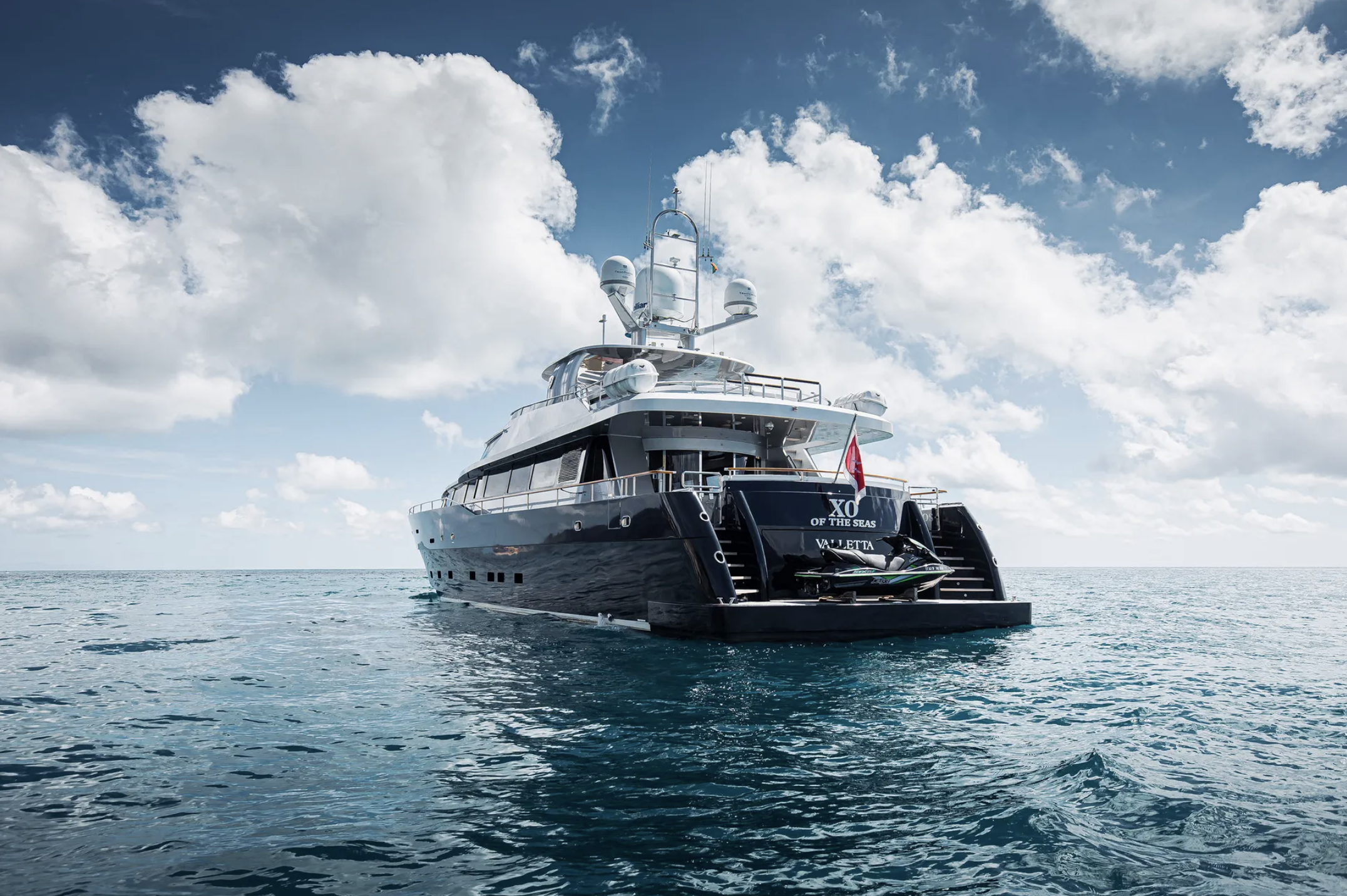 Large black yacht named 'XO OF THE SEAS' floating on calm ocean waters under partly cloudy sky.
