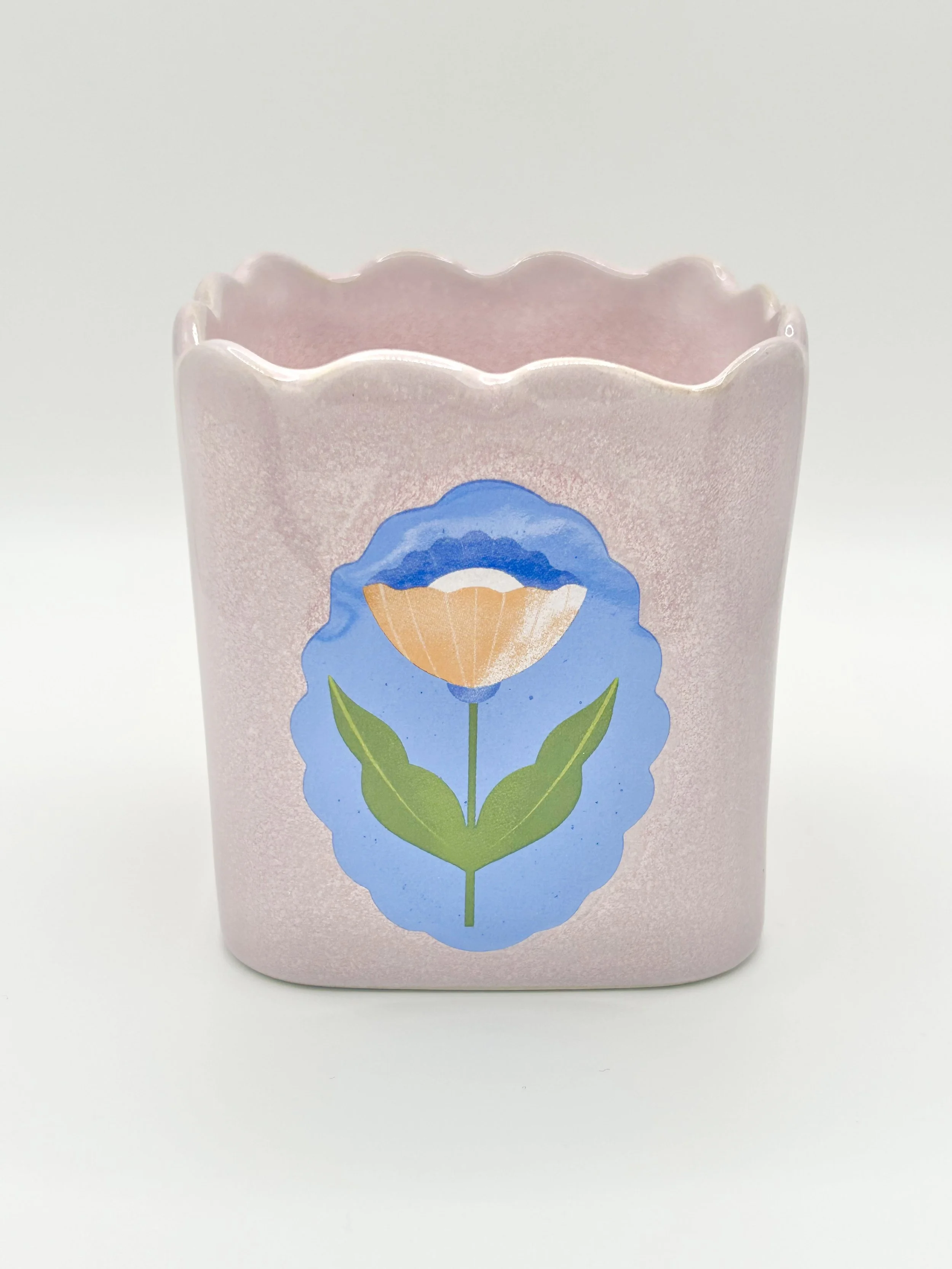 Decorative pink ceramic container with a scalloped top edge, featuring a painted blue and orange flower with green leaves on the front.