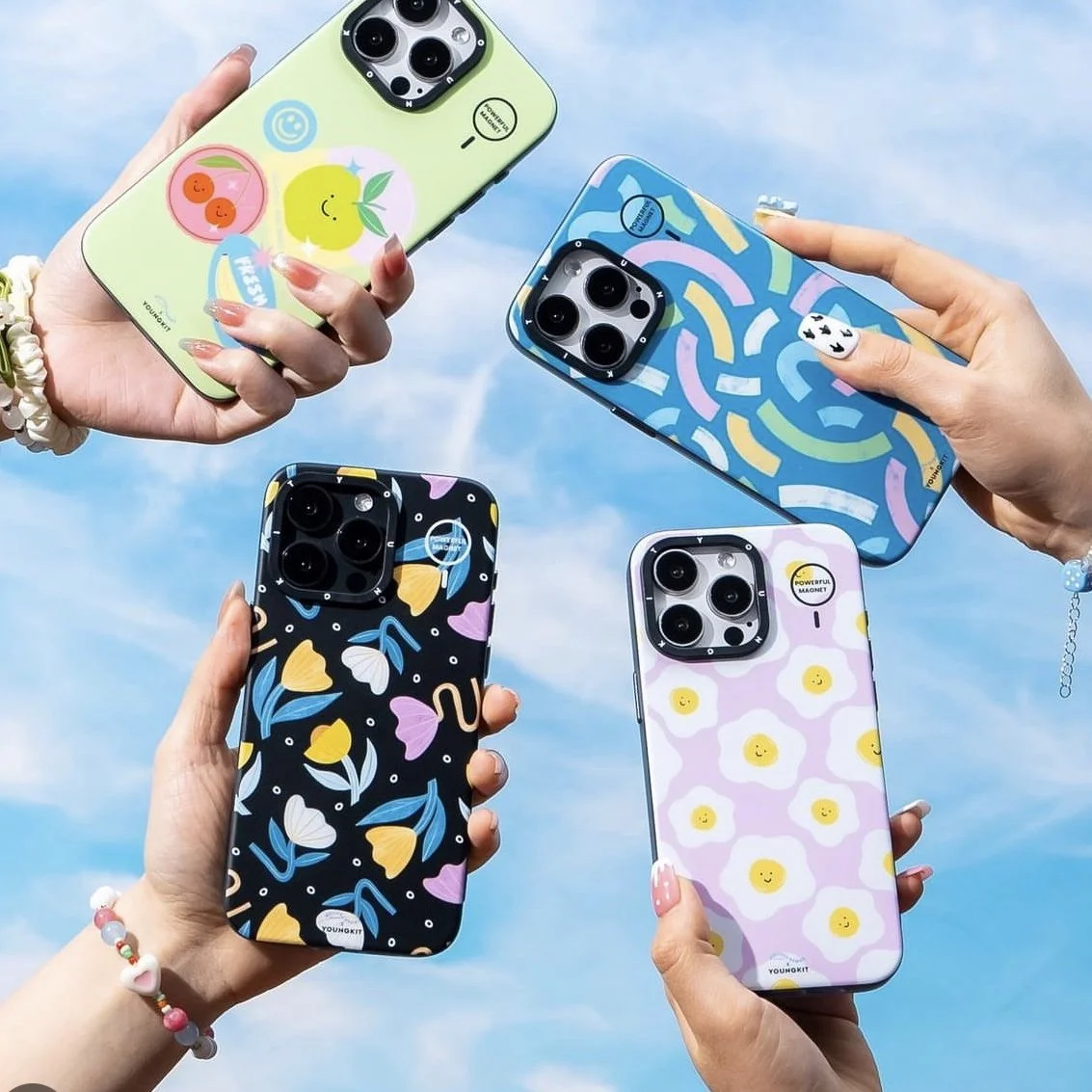 Four colorful smartphones with playful, patterned cases held up against a blue sky with clouds.