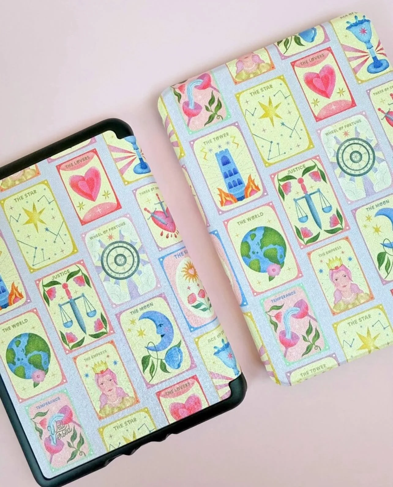 A phone and a notebook, both with pastel-coloured tarot card patterns, on a light pink background.