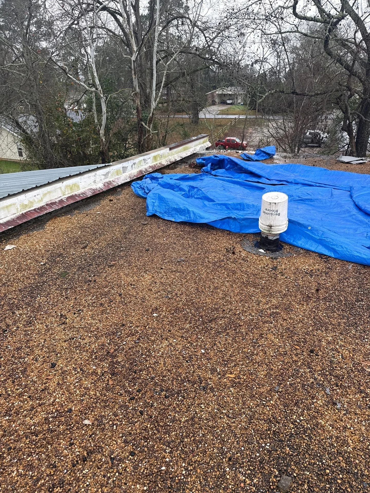 Flat rooftop with brown gravel surface, covered with blue tarps and a white vent pipe.