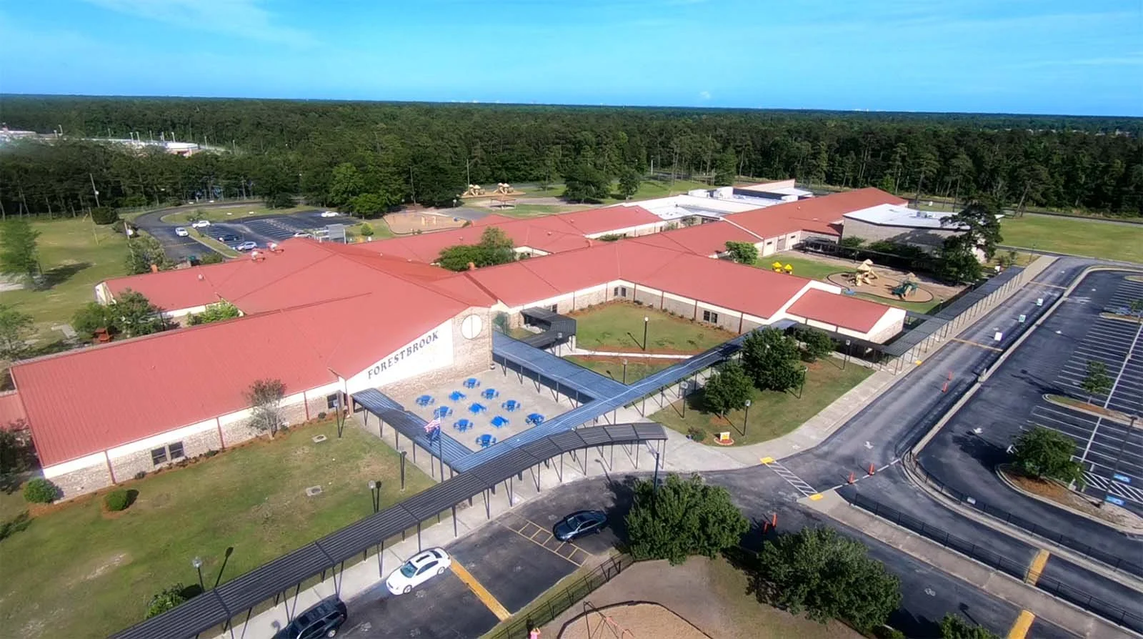 Aerial view of Foresterbrook school with red roofs, parking lot, playground equipment, and surrounding greenery.