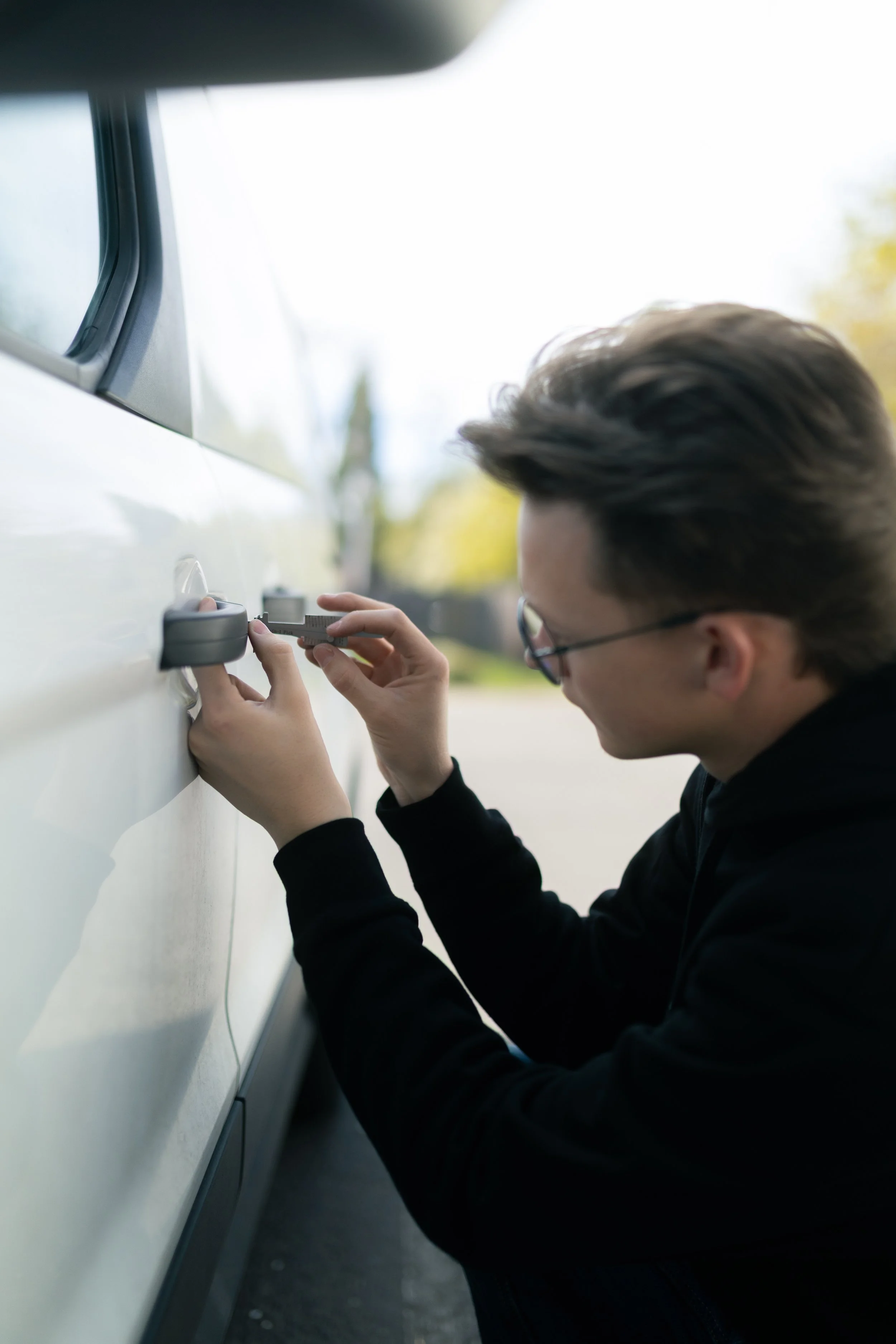 A person attaching a lock to a white vehicle, possibly a car, outdoors during daytime.