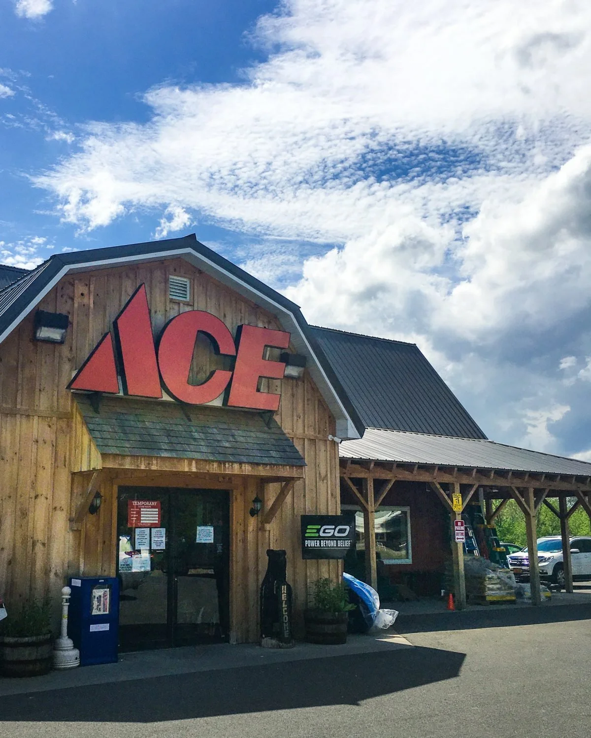 Exterior of an ACE hardware store with a large red ACE sign on a wooden building, under a partly cloudy sky.