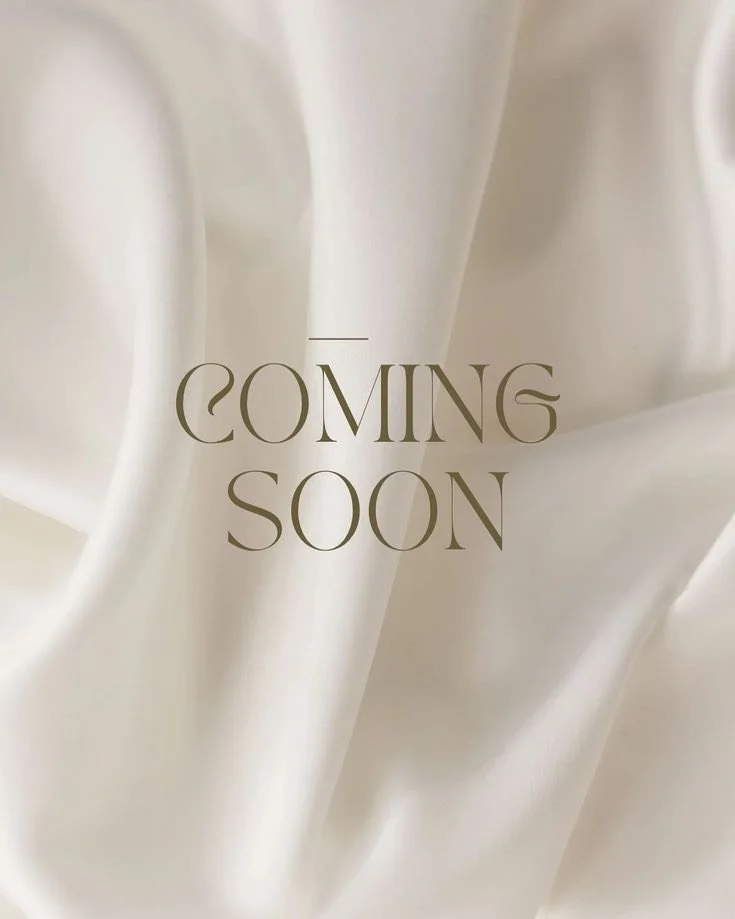 Text on a light-colored, silky fabric background that reads 'Coming Soon'.