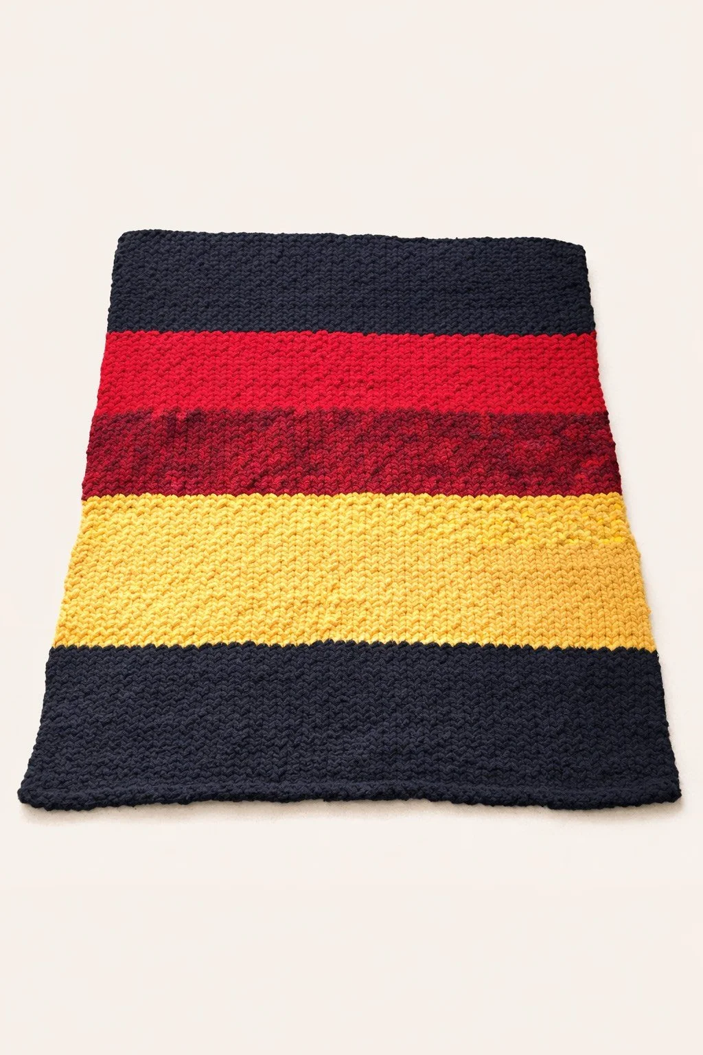 A knitted rectangular piece with horizontal stripes in black, red, maroon, yellow, and black colors.