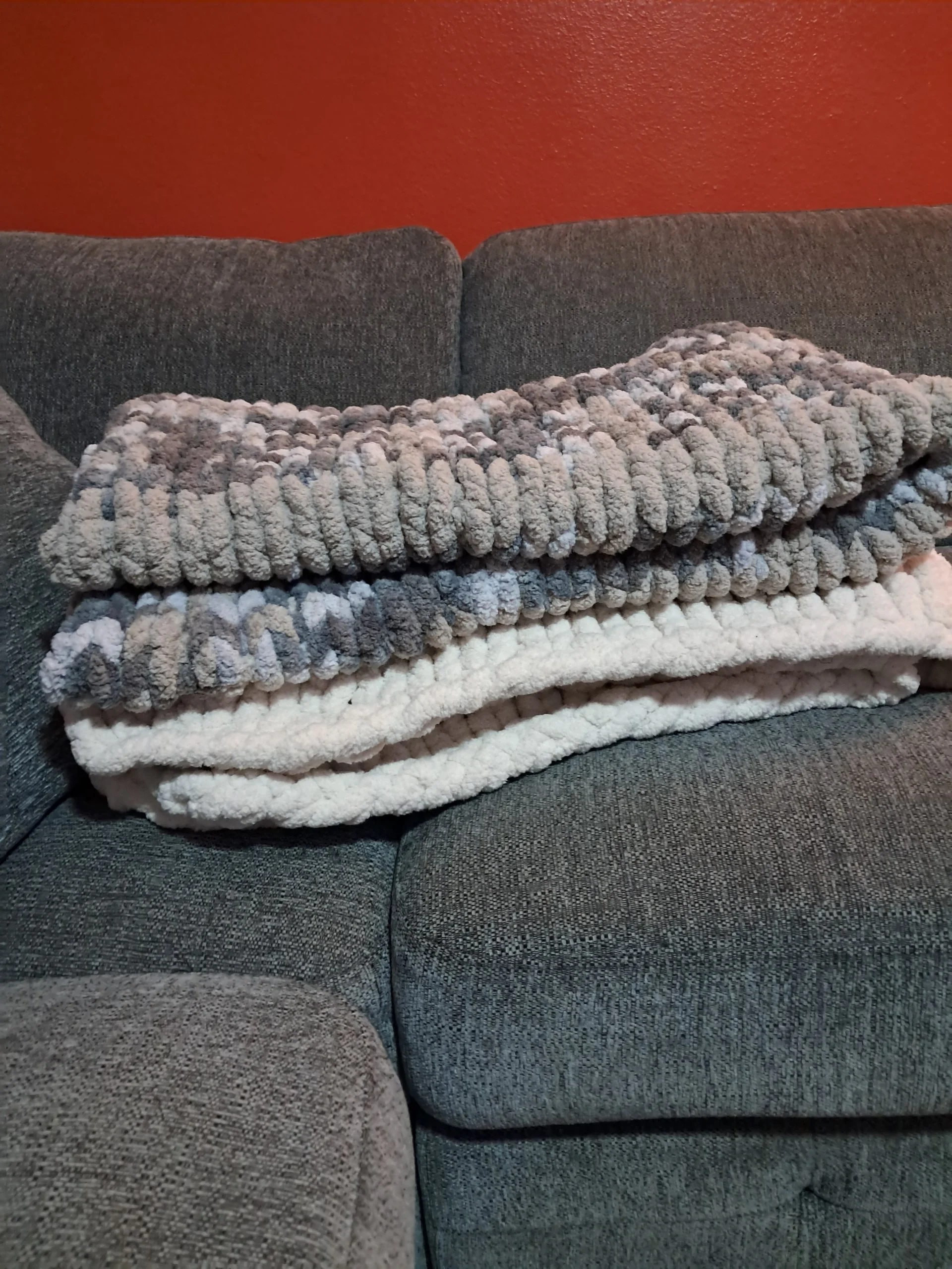 A gray textured sectional sofa with a plush, fluffy fleece blanket folded on the armrest, against a red wall.