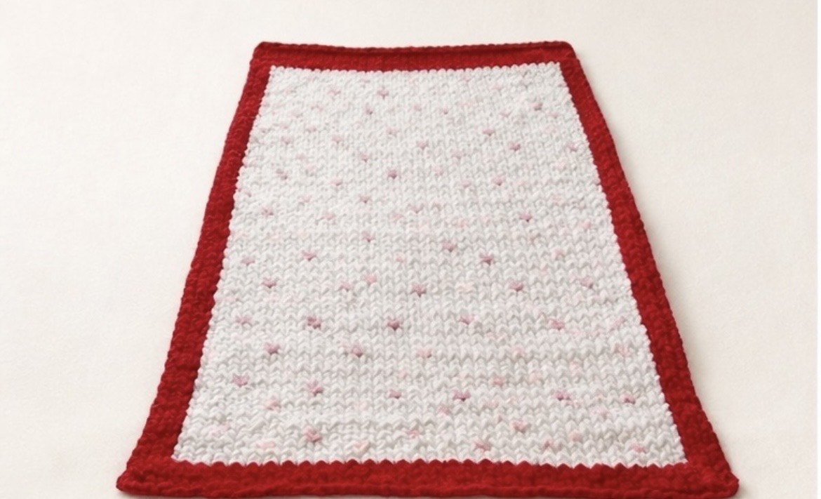 Red border white knitted rug with pink and white hearts.