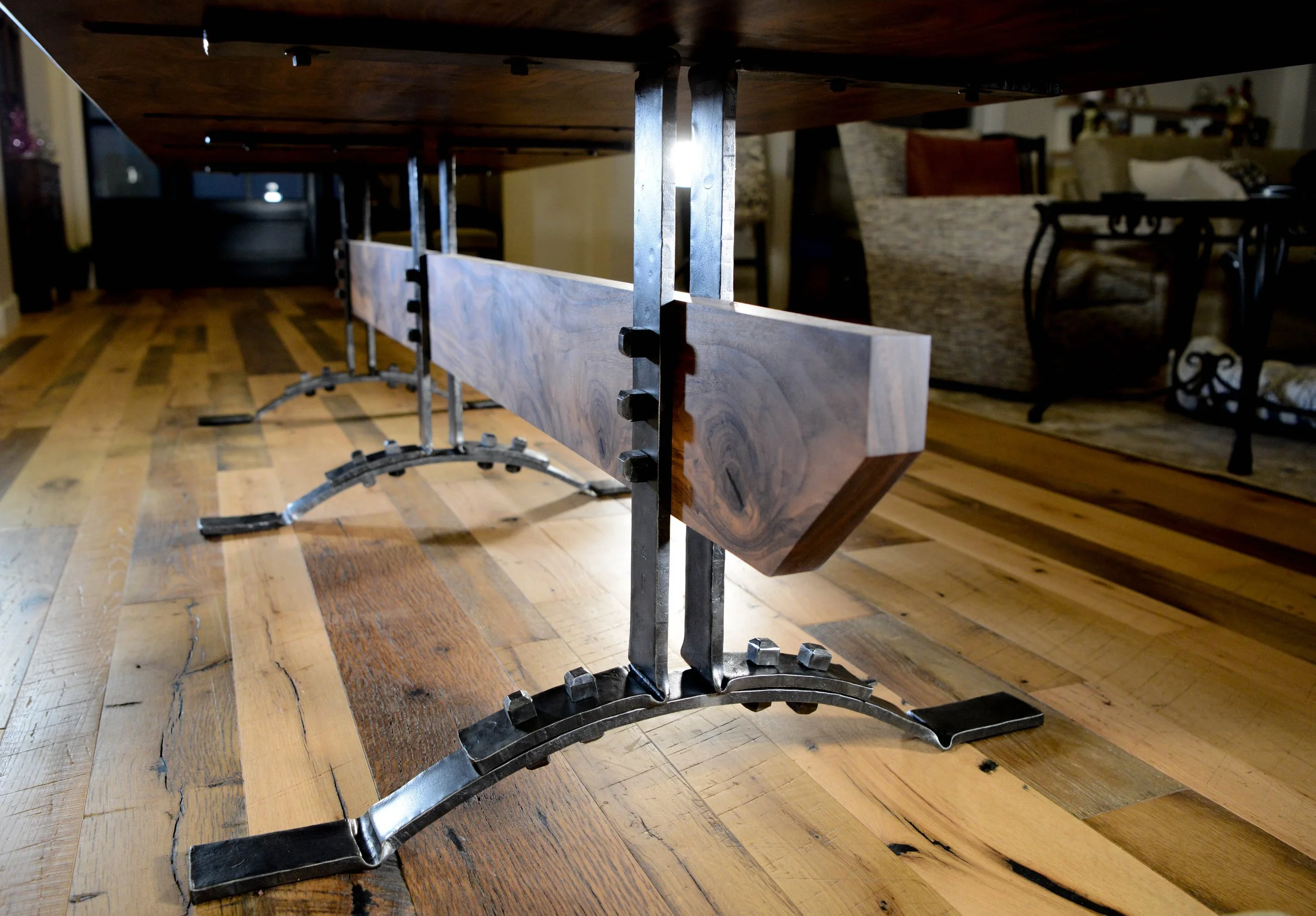 Close-up view of a wooden dining table with a metal support structure underneath, resting on a hardwood floor in a living room.