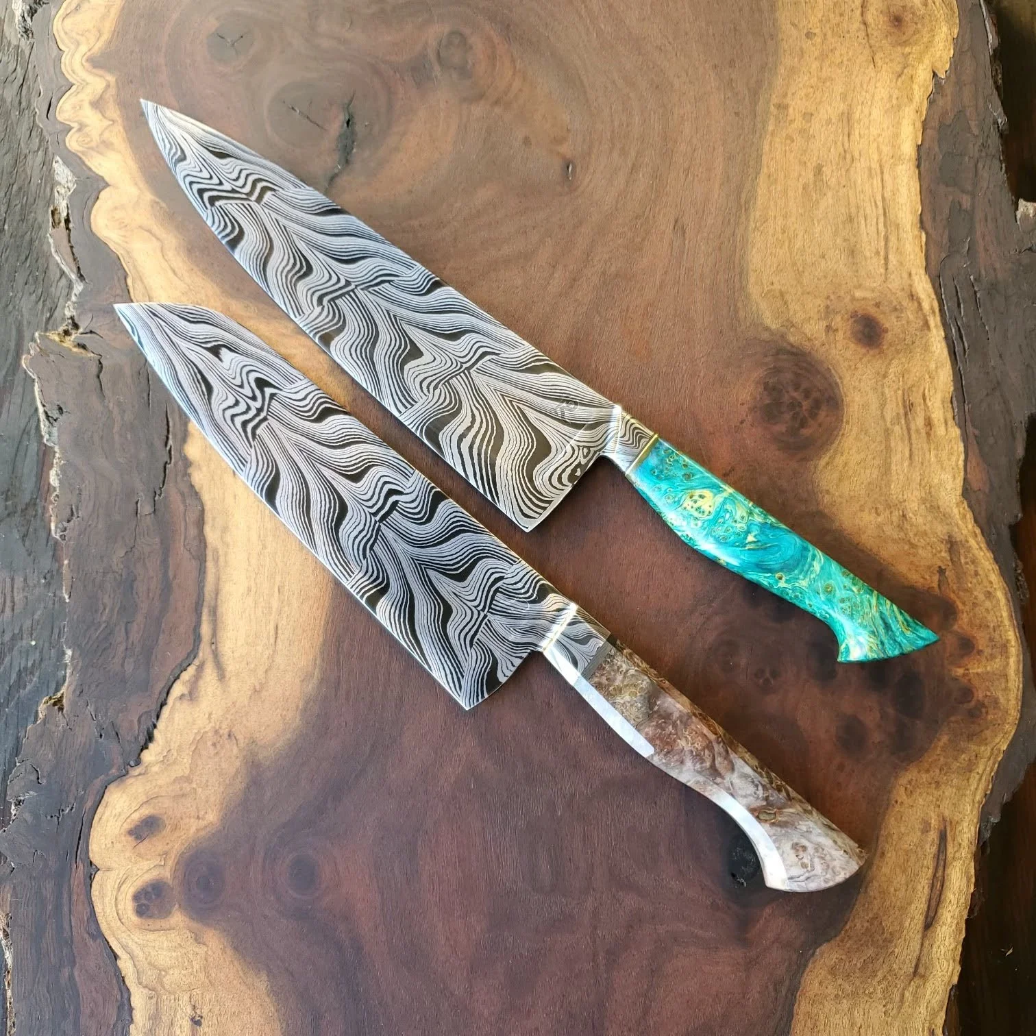 The “Whale Tail” damascus pattern by Mareko Maumasi, forged by me. Bottom knife is by Justin of Runningman Forge, the top one is mine. 1084 and 15n20 steel. Handles are dyed maple burl (2024)