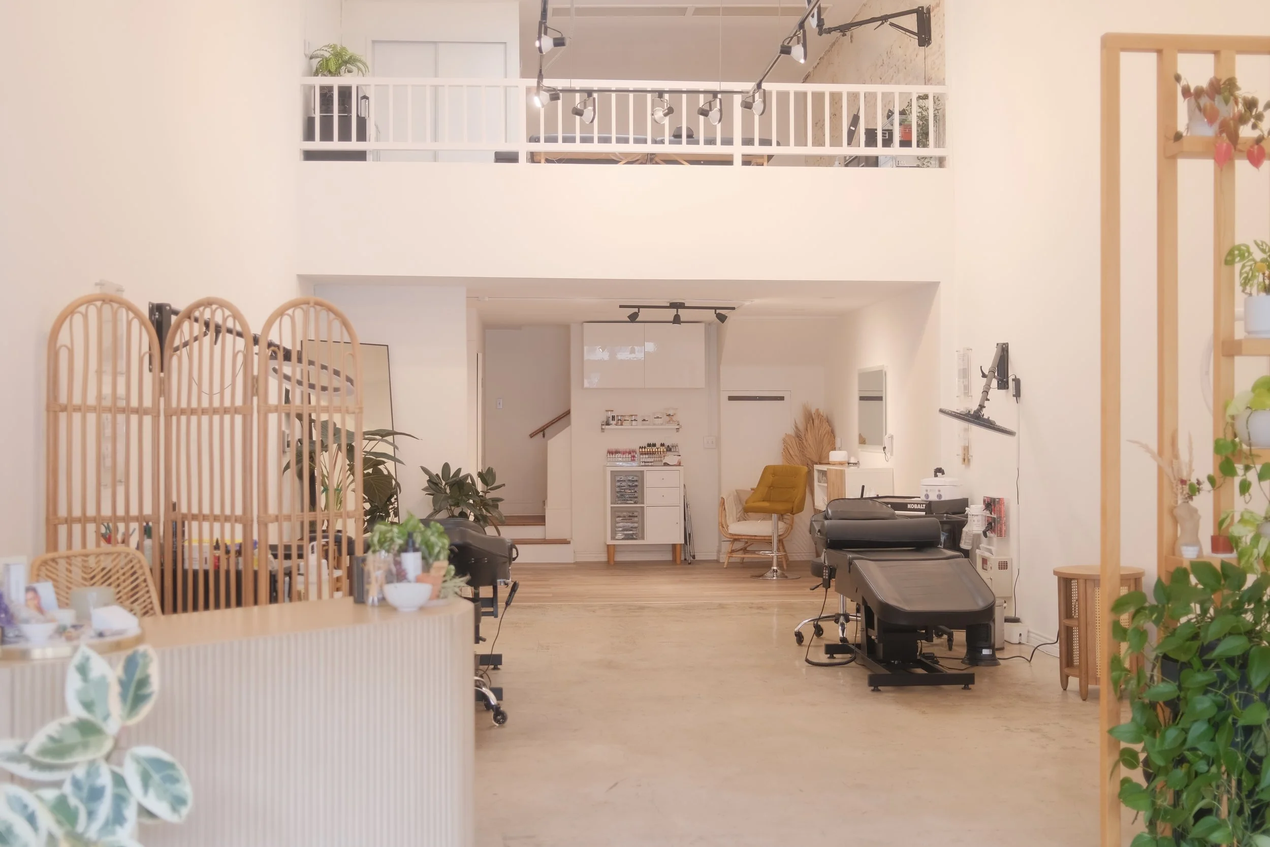 A overview image of Wildflower Beauty + Brows studio. A spacious, well-lit interior space with a high ceiling featuring black track lighting and modern decor.