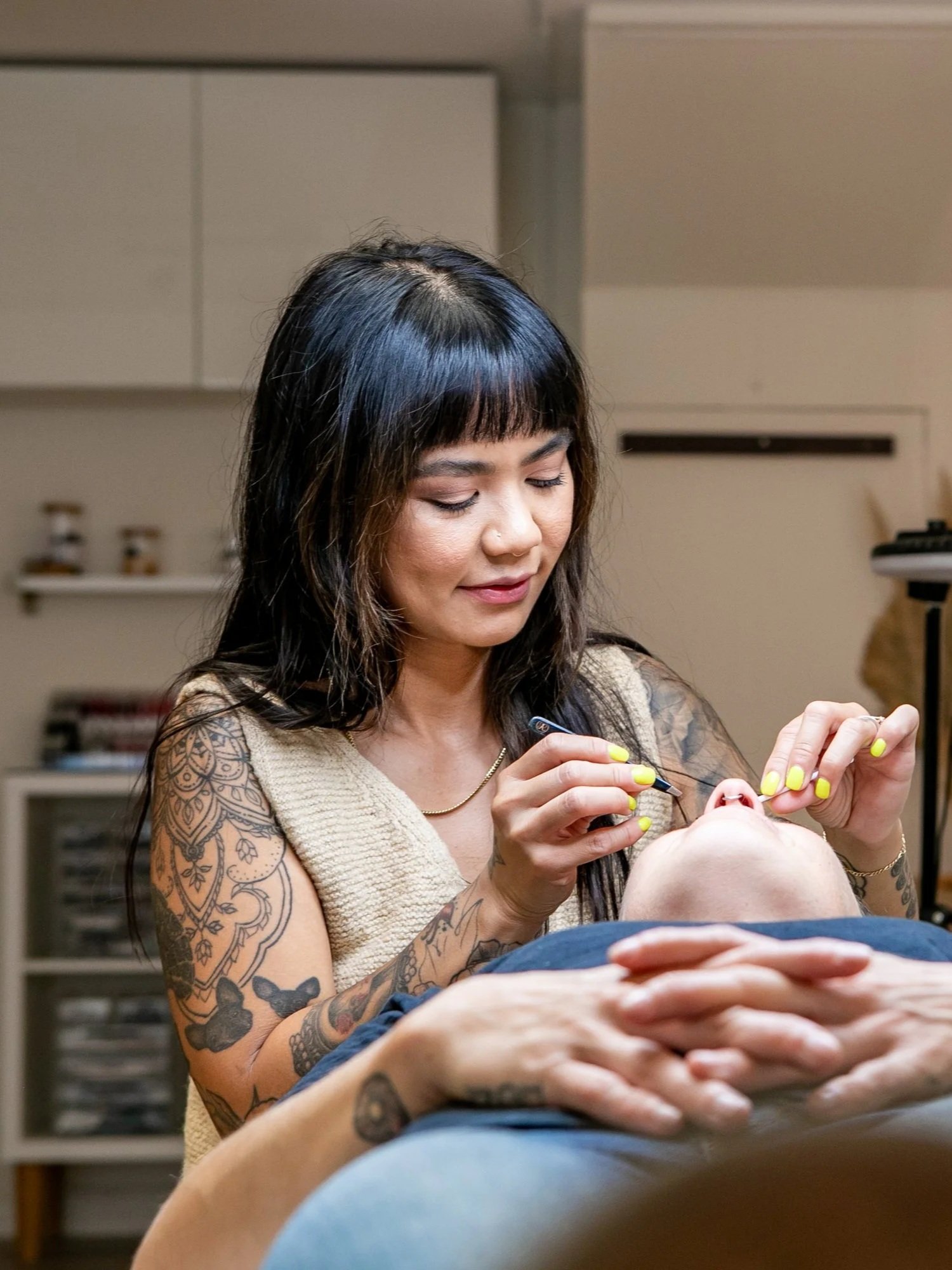 Rachelle is performing a cosmetic or medical procedure on a person's eyebrows, who is lying down with their eyes closed.