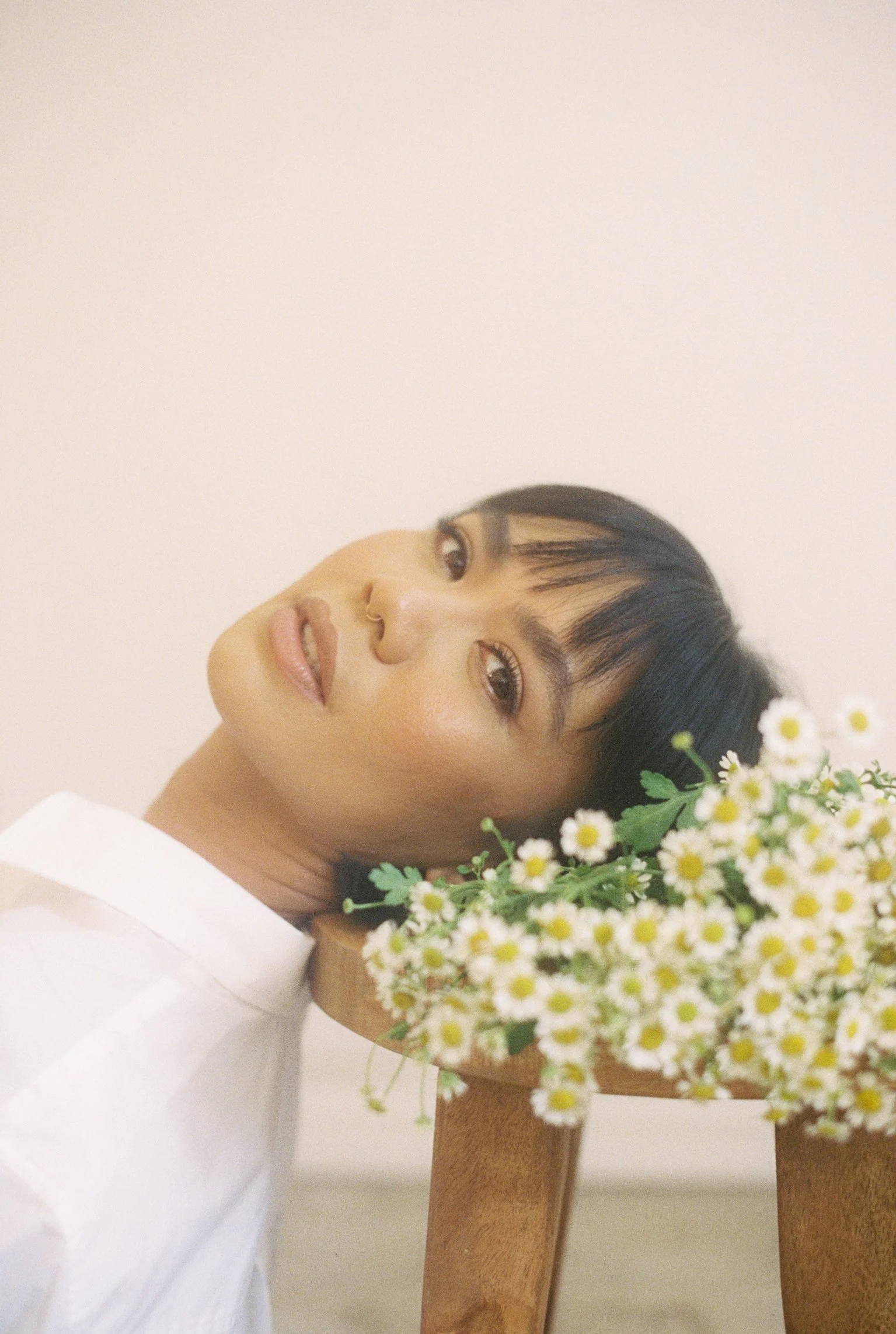 Rachelle lying down, looking at the camera, with a large bouquet of white daisies with yellow centers in front of her.