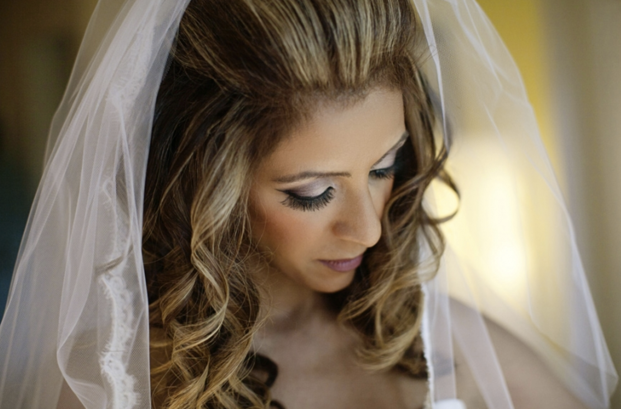 Close-up of a bride with styled hair, makeup, and a sheer veil with lace border.