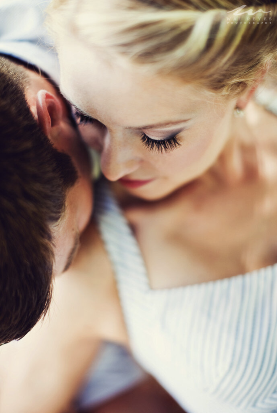 Close-up of a woman with blonde hair and long eyelashes leaning close to a man with dark hair, both appearing intimate and affectionate.