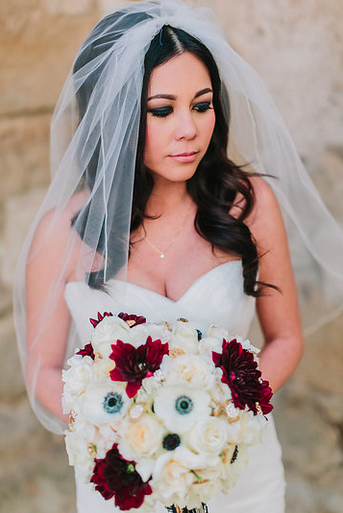 Bride in wedding dress with veil holding a bouquet of white and red flowers