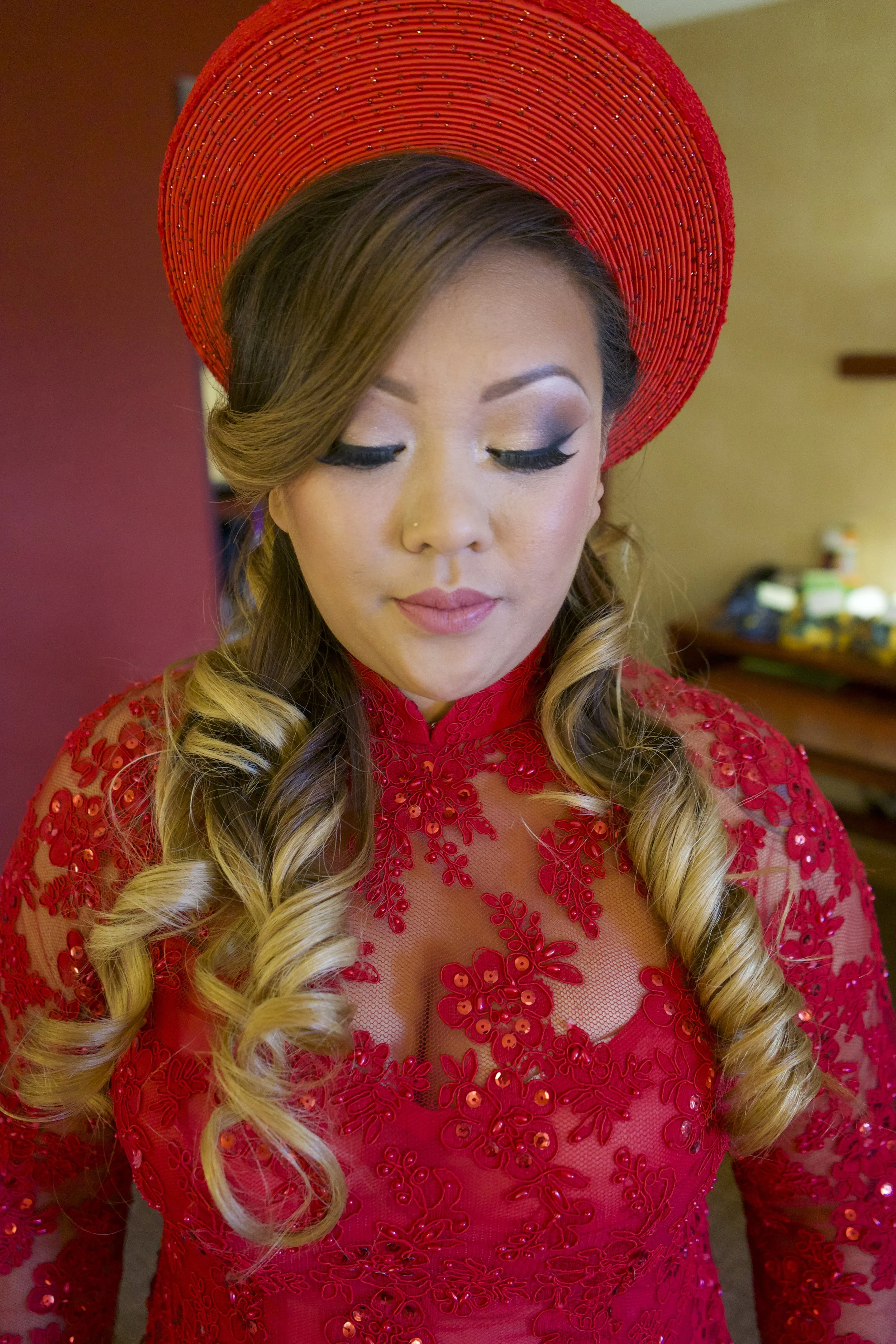 A woman with long, styled hair wearing a red, embroidered dress and a large matching red hat.
