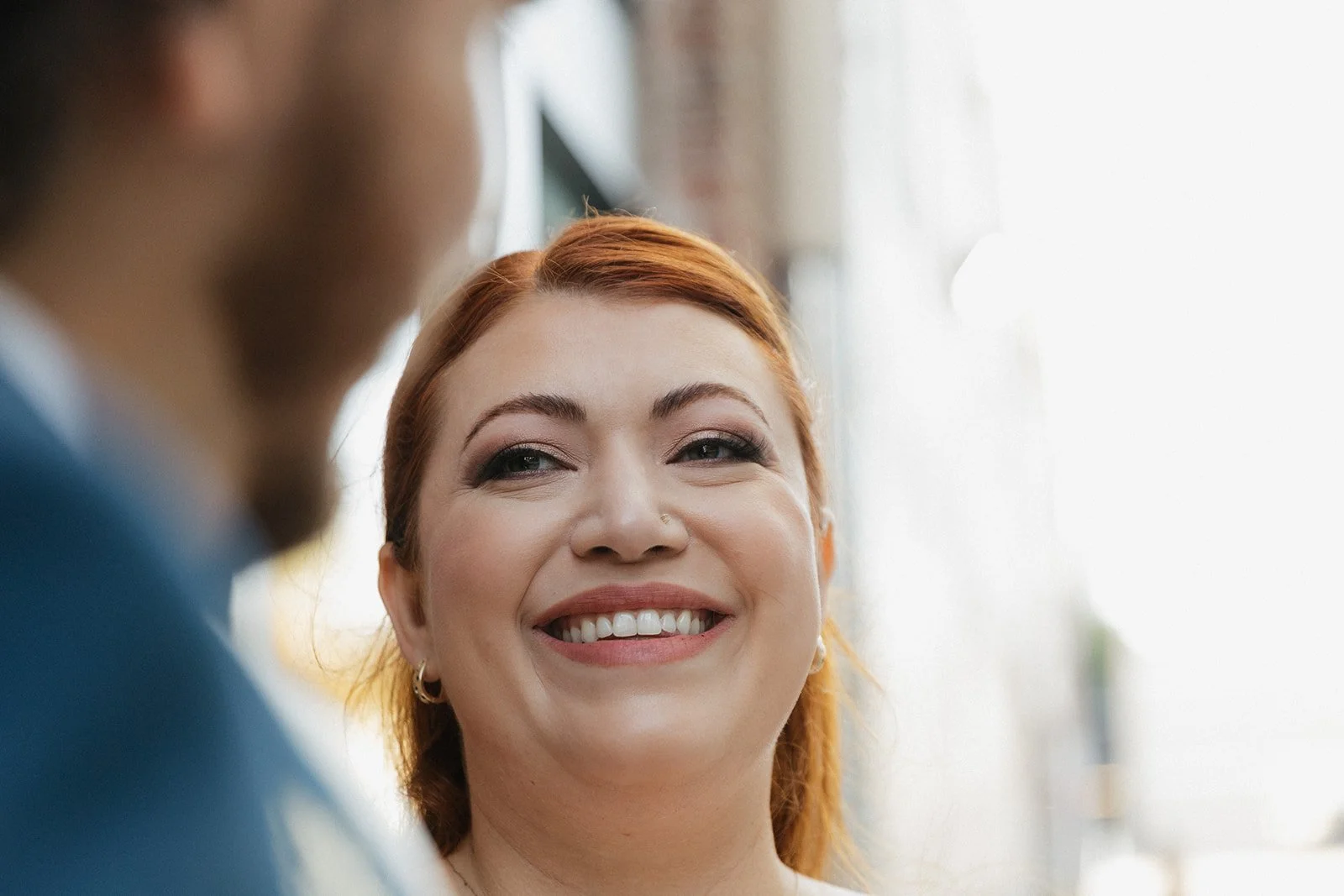 A woman with red hair smiling at a person whose face is partially out of focus in the foreground.