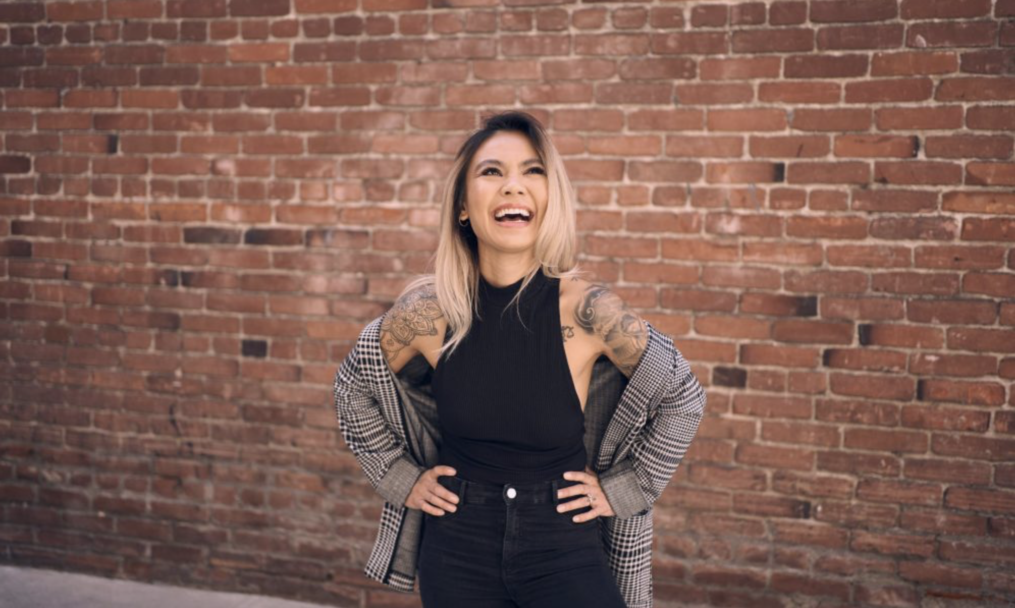 Rachelle standing in front of a red brick wall, laughing with her hands on her hips.