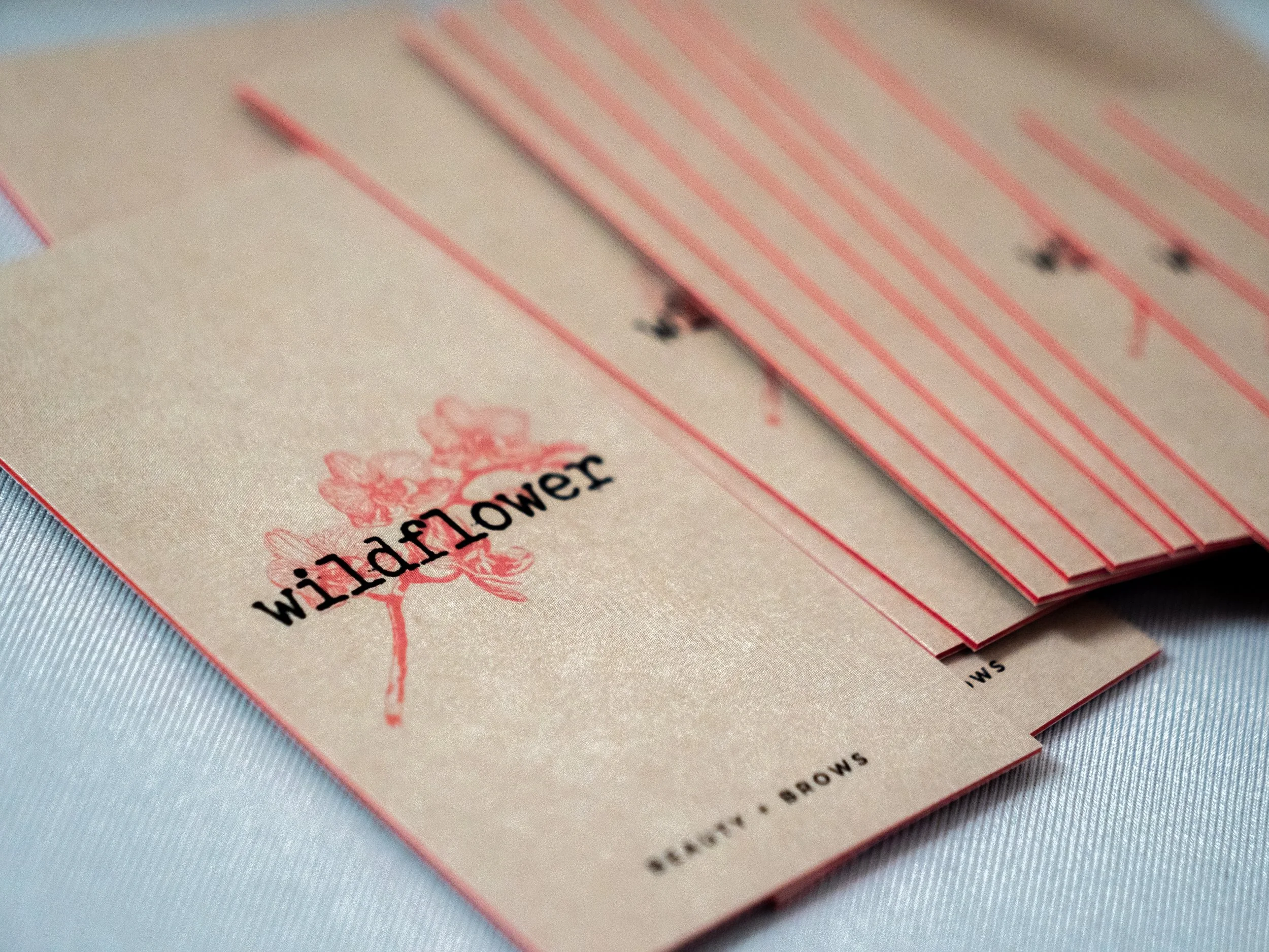 Close-up of business cards with red and white stripes and small black clasps at the bottom, resting on a beige paper surface with pink flower and text design.