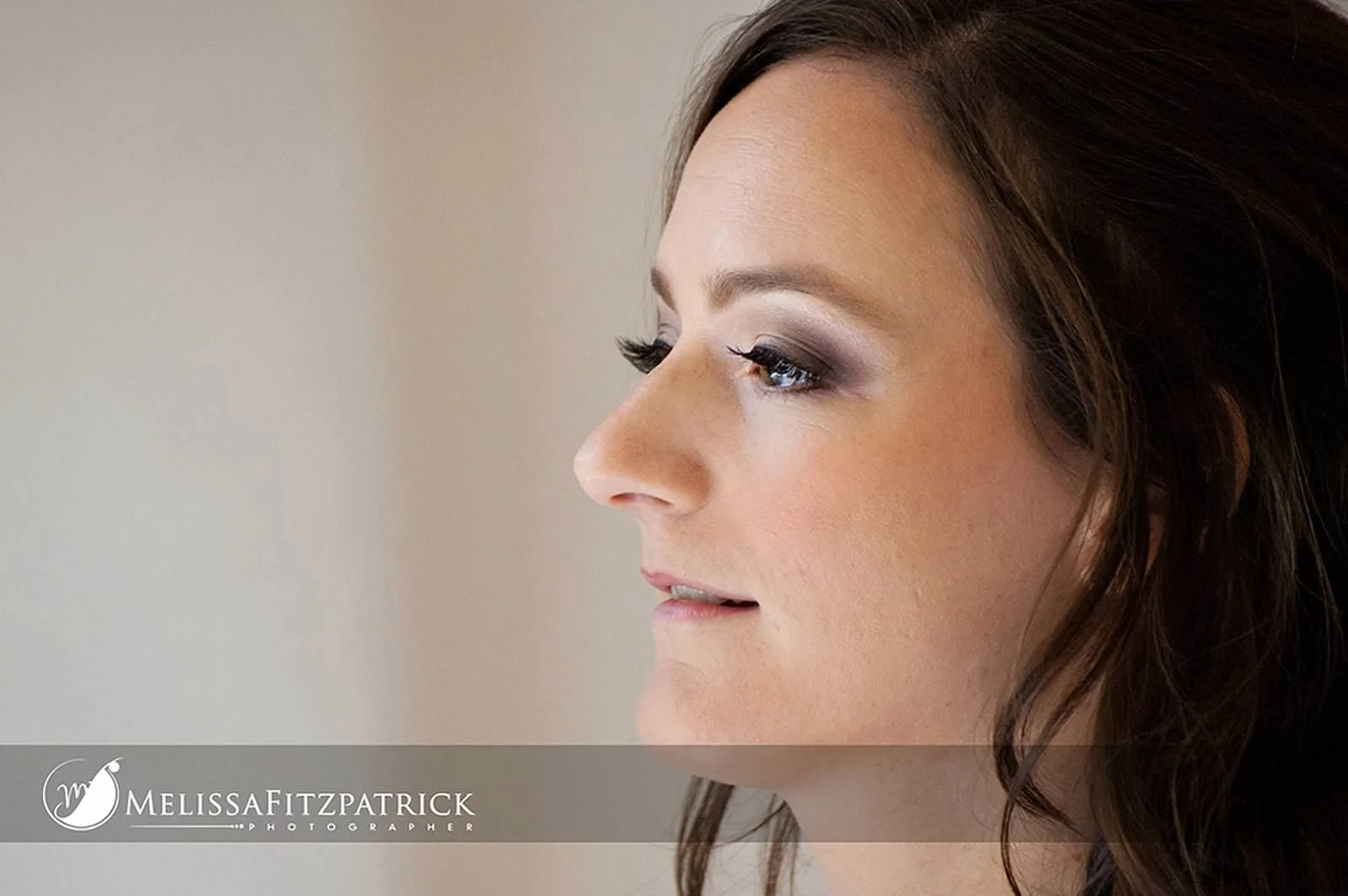 Profile view of a woman with brown hair and makeup, against a plain background, with a logo for Melissa Fitzpatrick Photography at the bottom.
