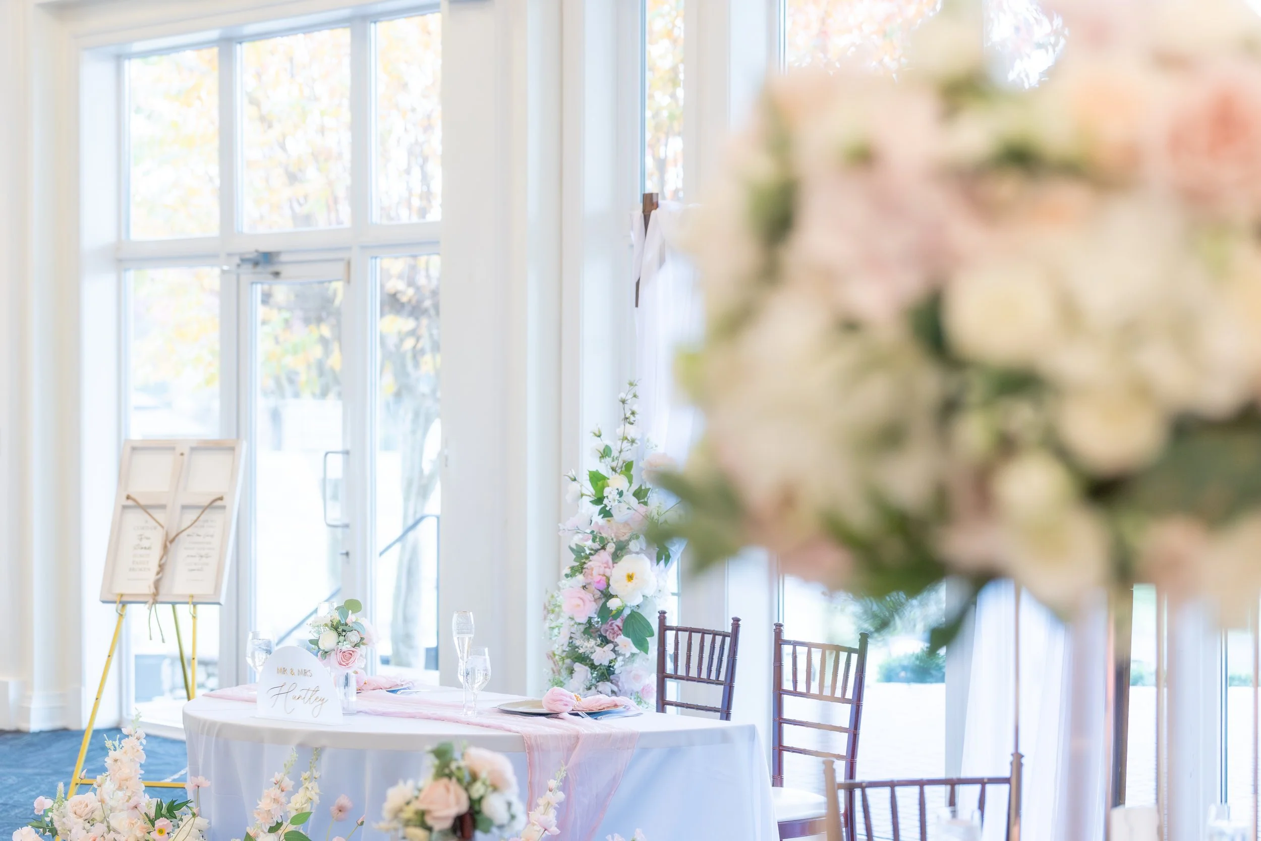 Wedding reception setup with a decorated table, floral arrangements, and a large window in the background.