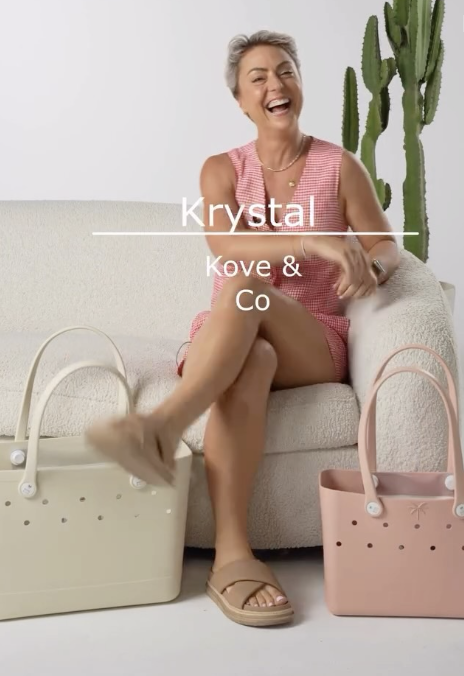 A smiling woman in a pink checkered outfit sitting on a beige couch, with large potted cactus plants in the background, two shopping bags in front, and the text 'Krystal Kove & Co' on the image.