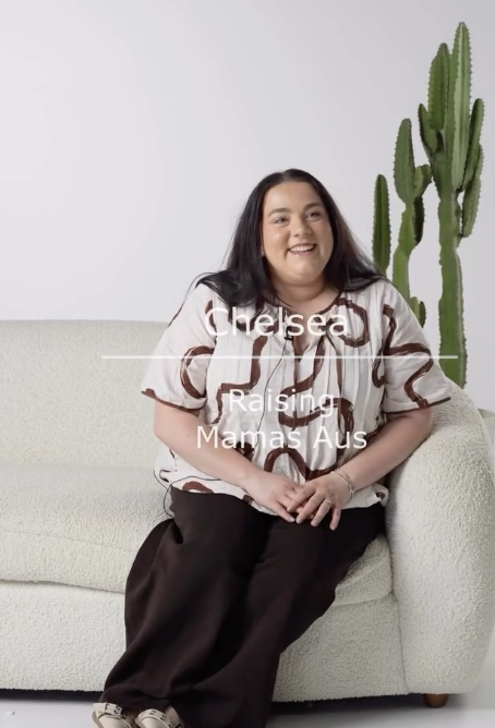 A woman with long dark hair smiling, sitting on a white sofa with a cactus plant in the background.