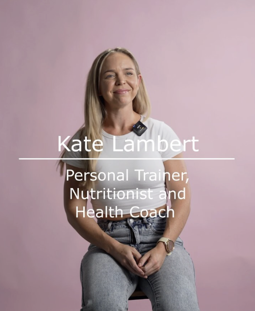 Portrait of Kate Lambert, personal trainer, nutritionist, and health coach, sitting against a pink background.