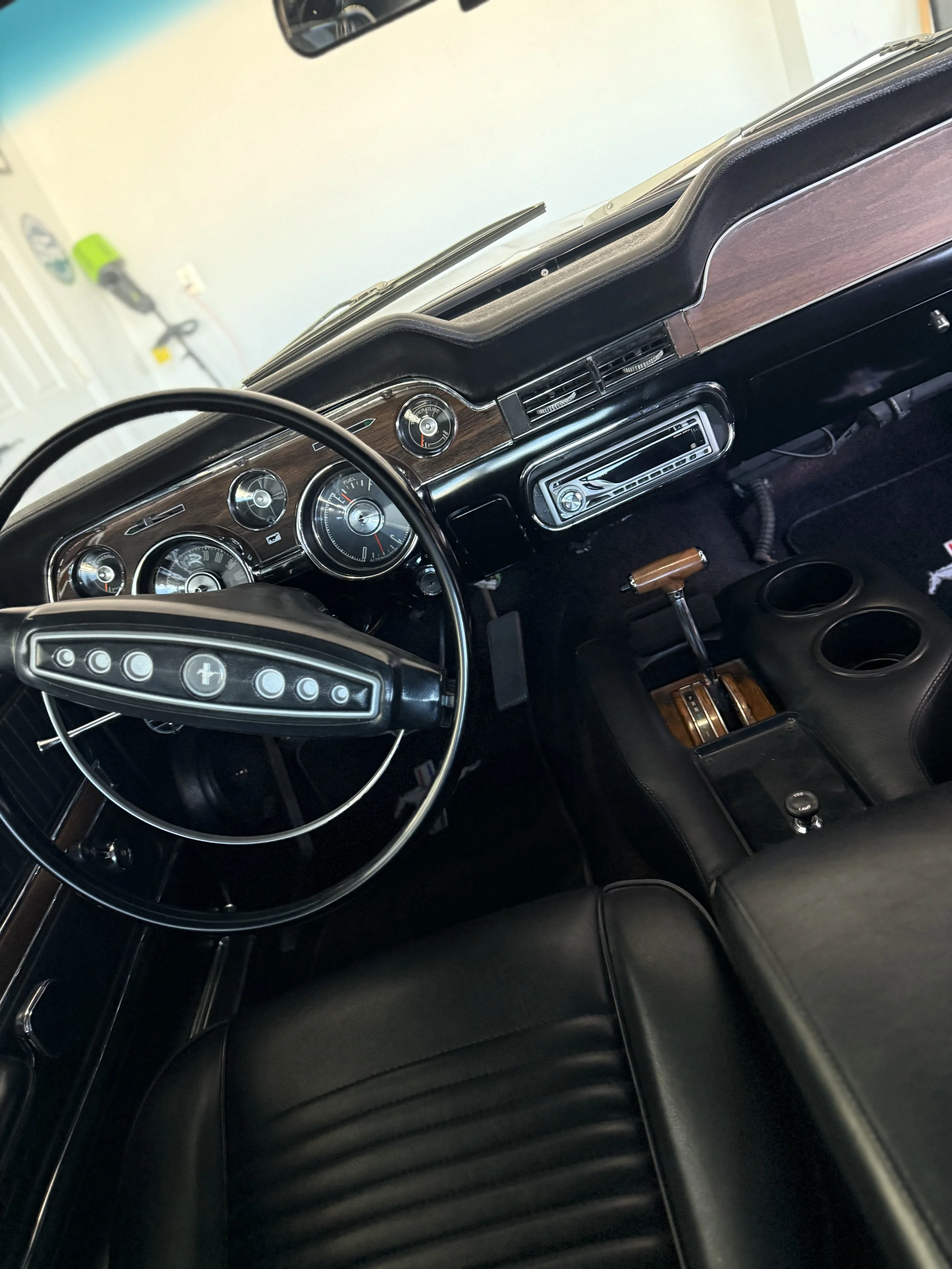 Interior of a vintage car dashboard and steering wheel with wood accents and analog gauges.